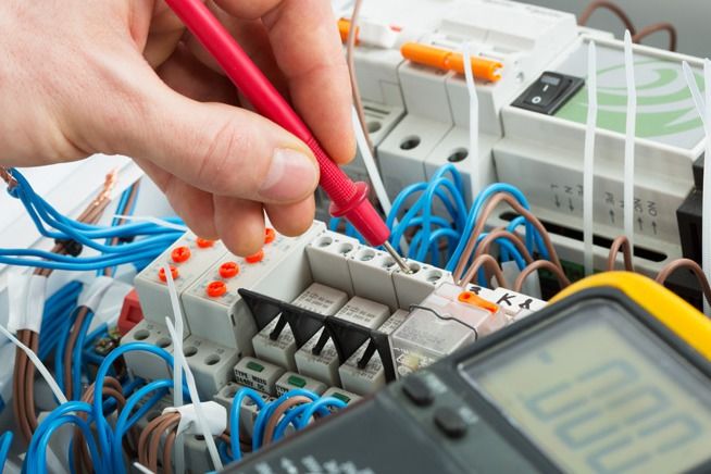 Hand of an electrician with multimeter probe at an electrical switchgear cabinet