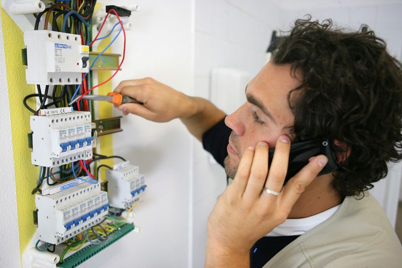 A certified electrician on the phone while working on circuit breakers