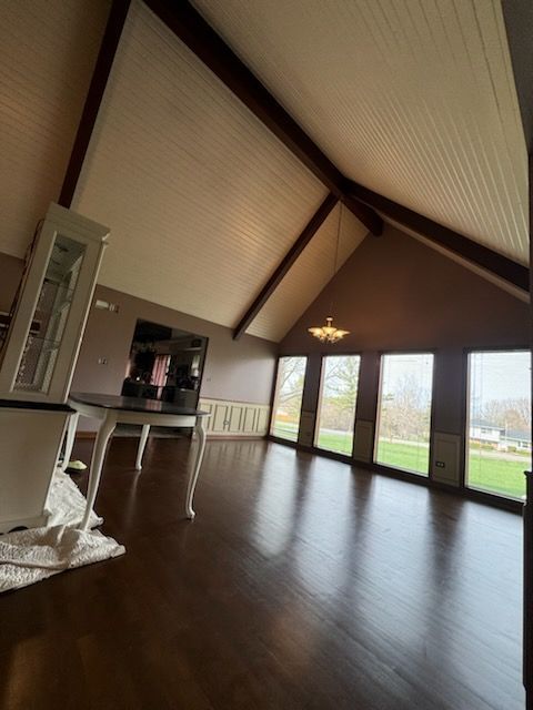Spacious loft with dark wood floors, high vaulted ceiling, and large windows overlooking a green yard