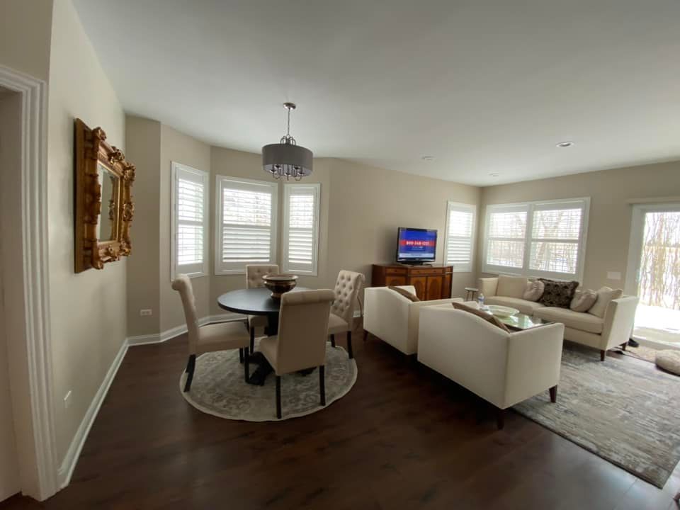 An open-plan room with neutral walls and dark floors, featuring a dining table, chairs, and two cream-colored sofas.