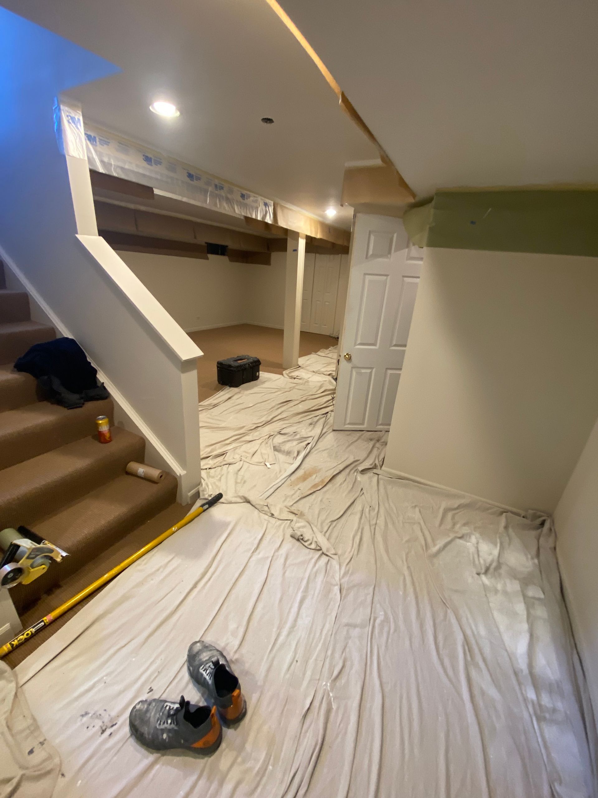A basement undergoing renovation with a drop cloth covering the floor, a wooden staircase, and a white door.
