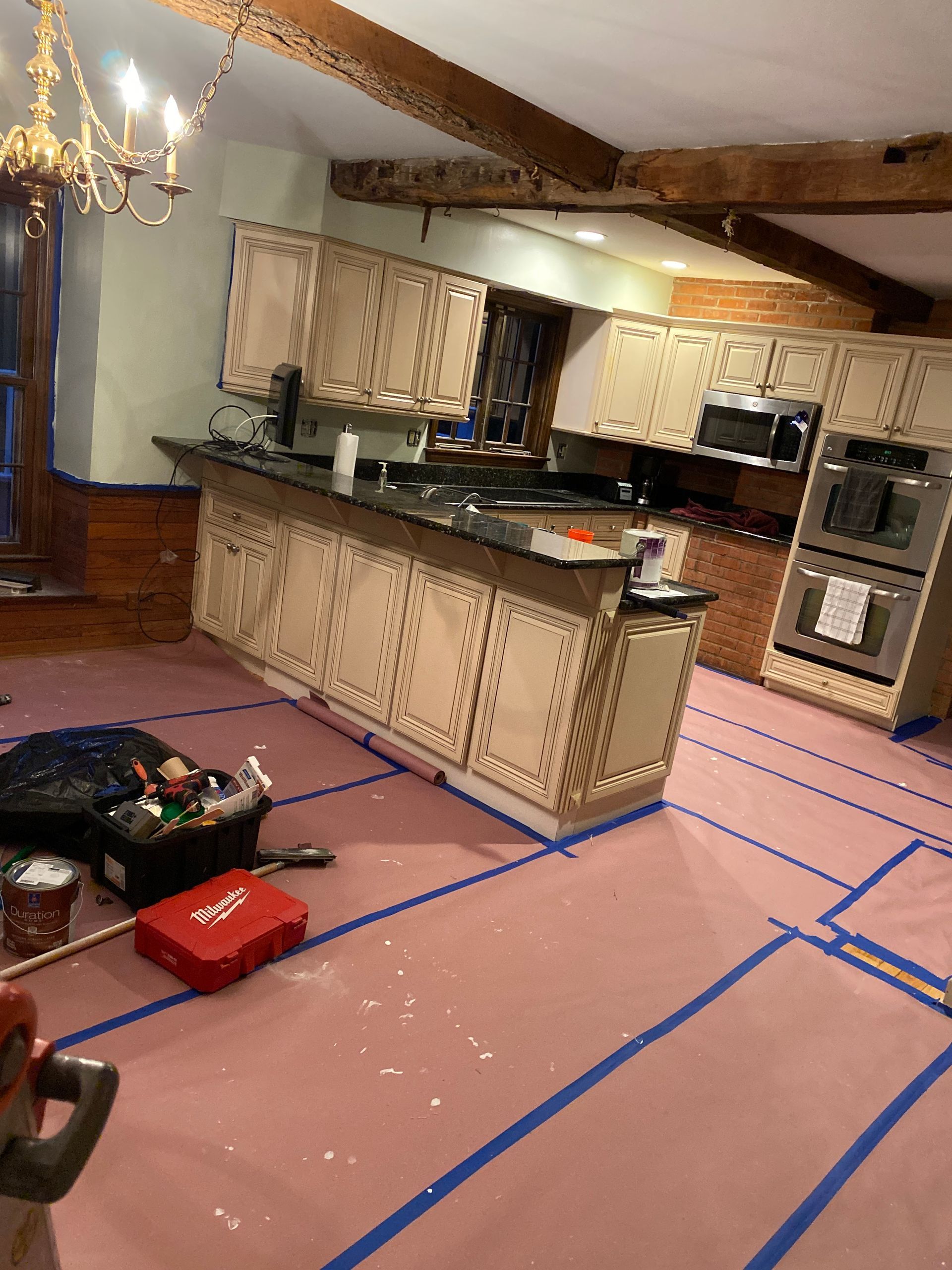 A kitchen undergoing renovation with light cabinets, a dark countertop, an island, and protective paper covering the floor.