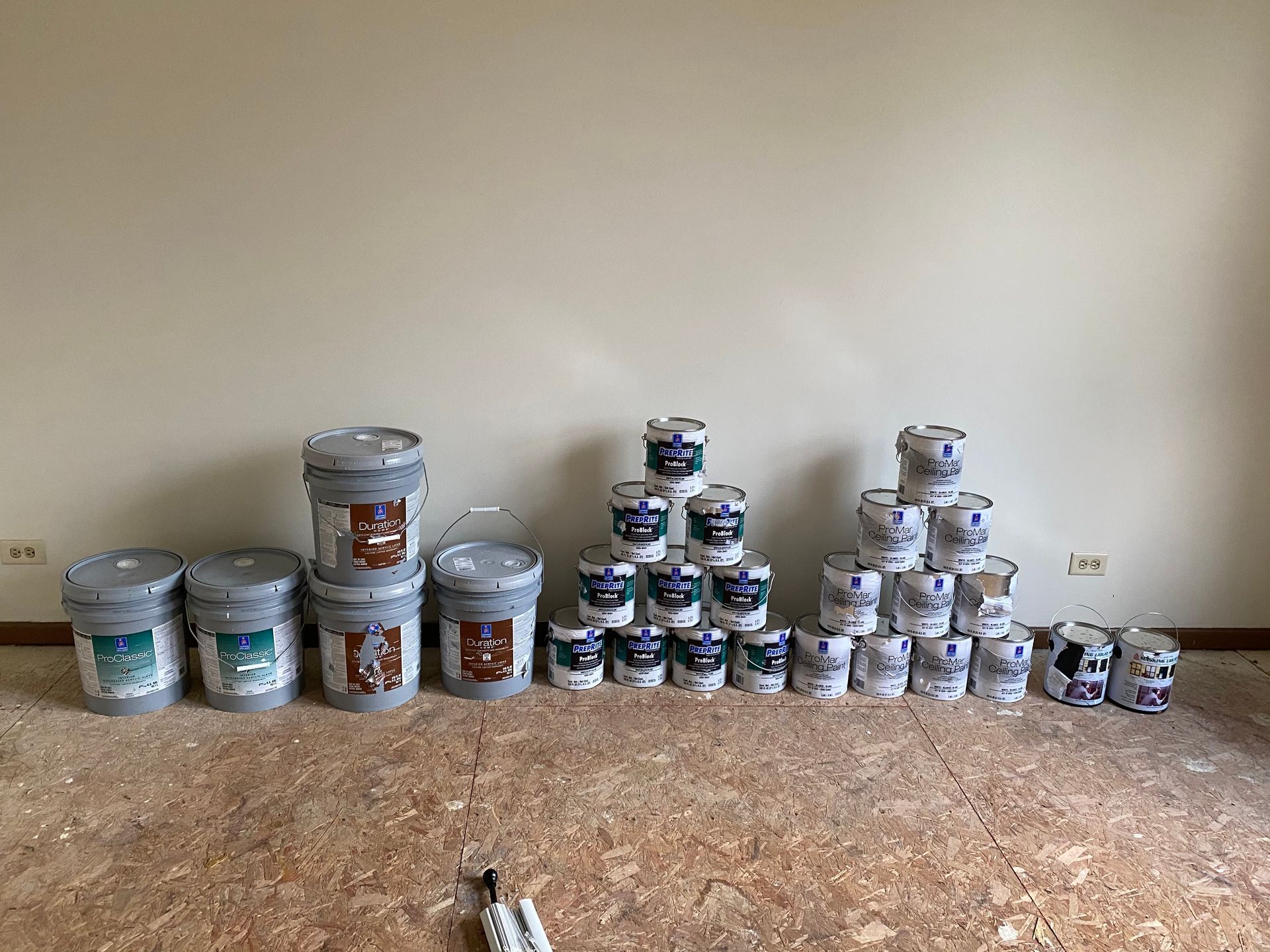 Various sizes of paint buckets arranged on a room floor against a plain wall.
