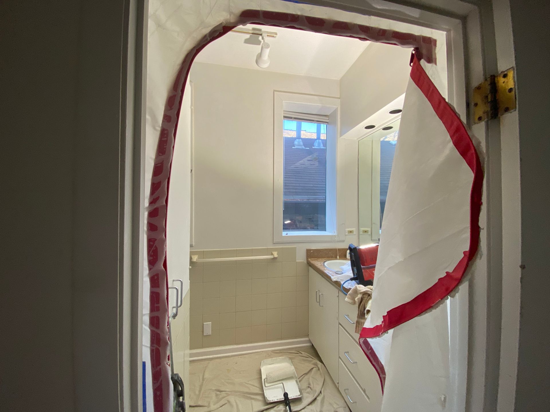 A white plastic dust barrier with a red trim installed in a bathroom doorway during a renovation.