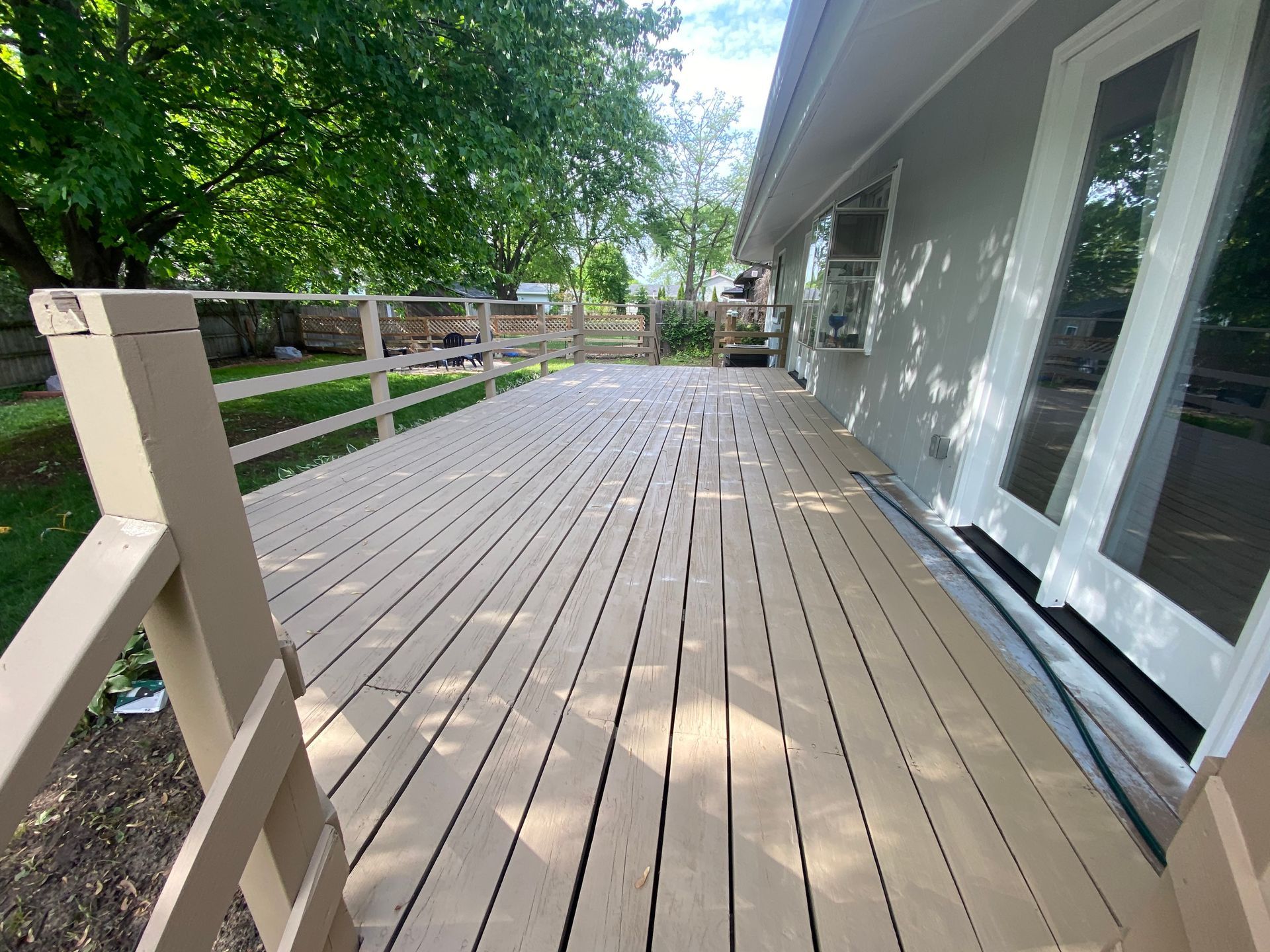 A light-colored wooden deck extends from the back of a house, featuring a simple railing overlooking a grassy yard.
