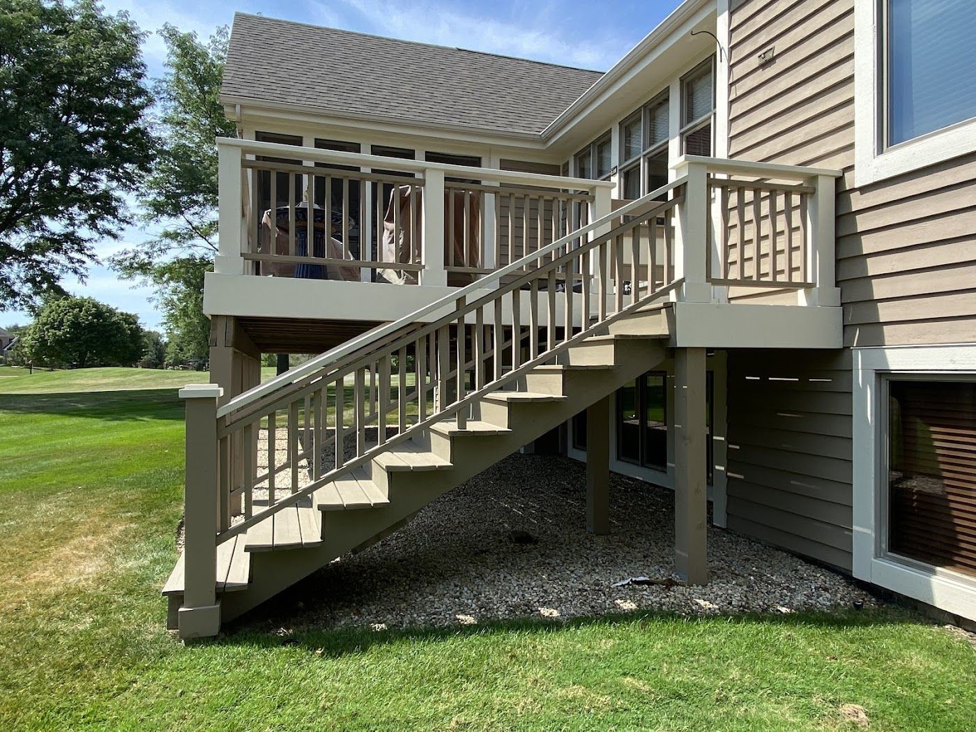 A tan-colored deck with stairs and white railings attached to a house with beige siding, overlooking a grassy lawn.