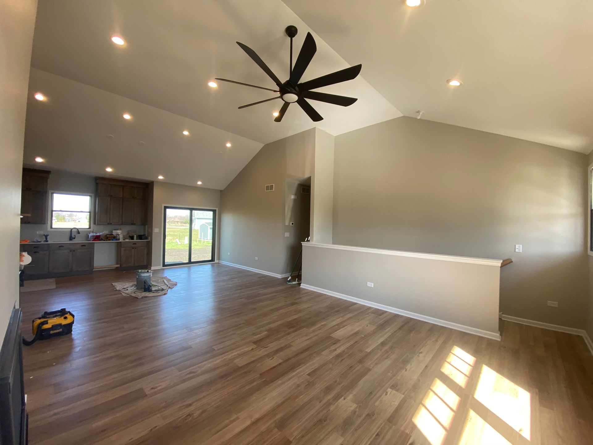 Wide-angle view of a bright, open-concept living area with vaulted ceilings, wood flooring, a ceiling fan, and kitchen.