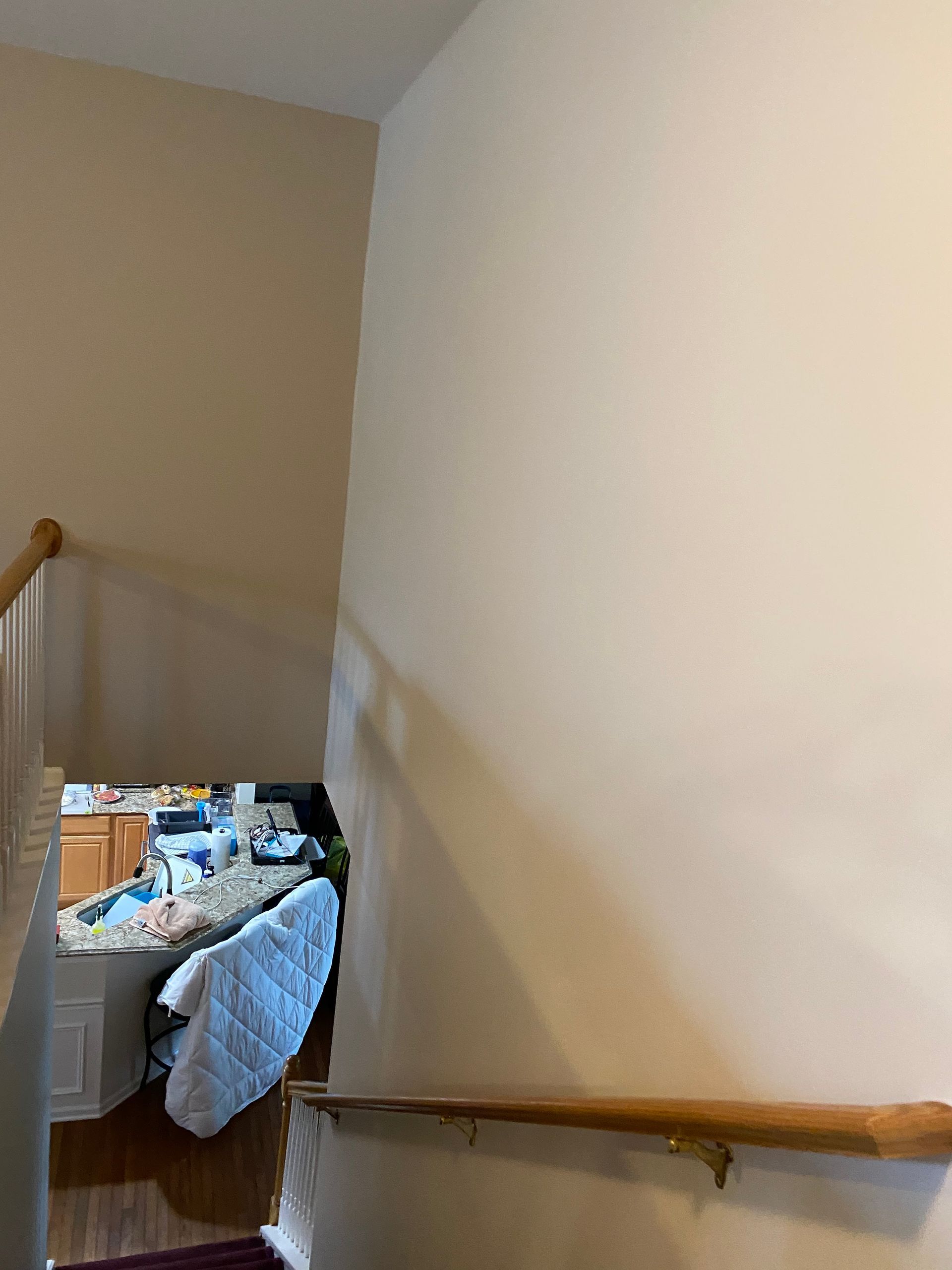 A view from the top of a staircase looking down into a home kitchen with granite countertops and a draped chair.