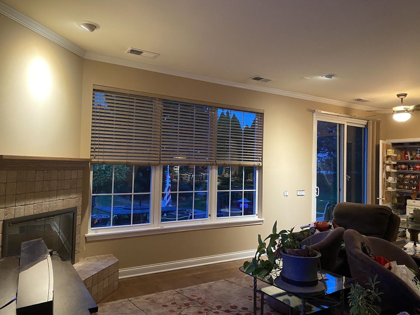 A cozy living room with a brick fireplace, large windows with horizontal blinds, and comfortable seating near a glass door.