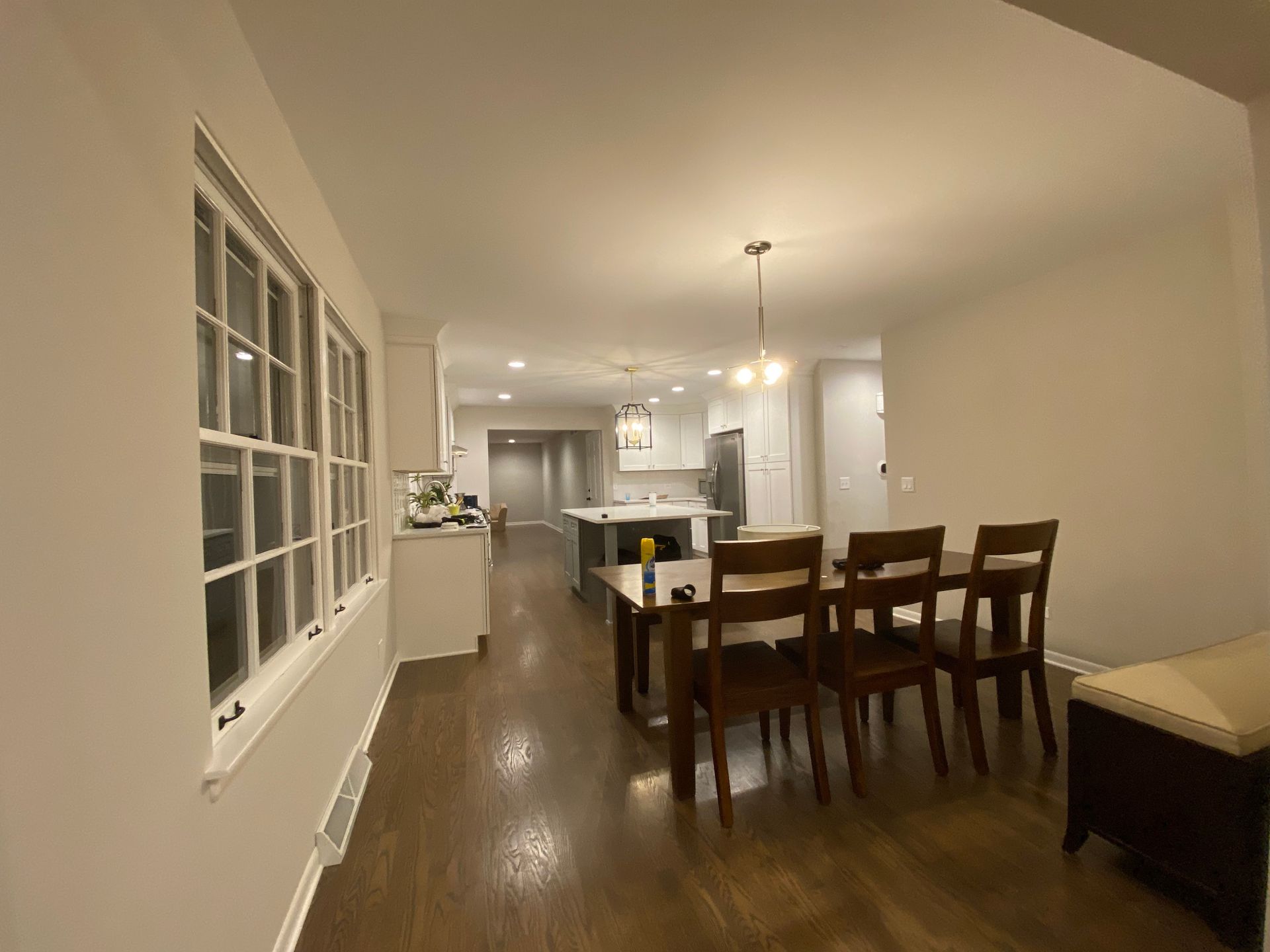 A bright, open-concept dining room with wood floors leads into a white kitchen featuring an island and stainless appliances.