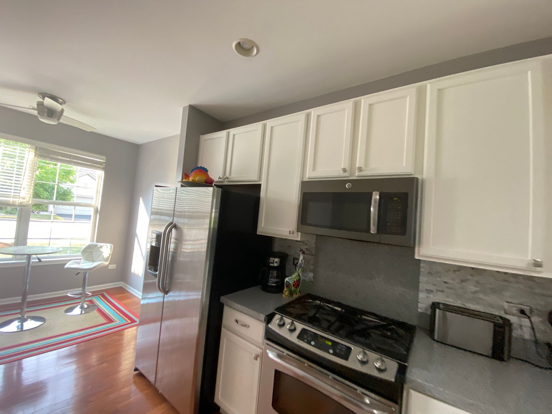 A kitchen interior with white cabinets, stainless steel appliances, a stove, a microwave, and a small dining area.