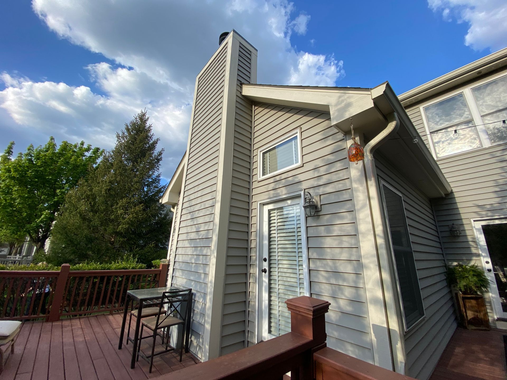 Light gray horizontal siding on a house exterior featuring a tall chimney, a back door, and an attached wooden deck.