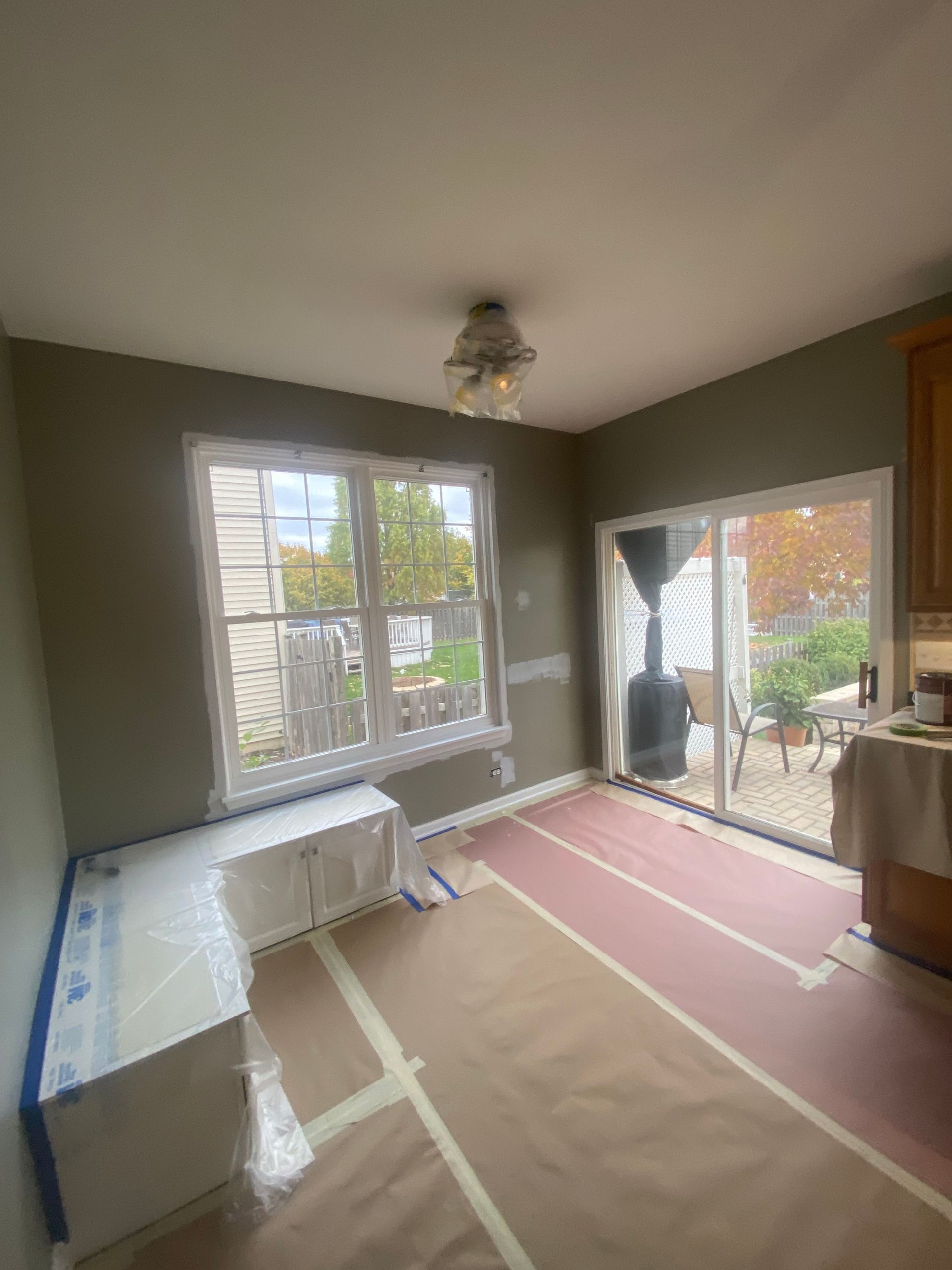 A room under renovation with gray walls, a window covered in plastic, papered floors, and a glass sliding door to a patio.
