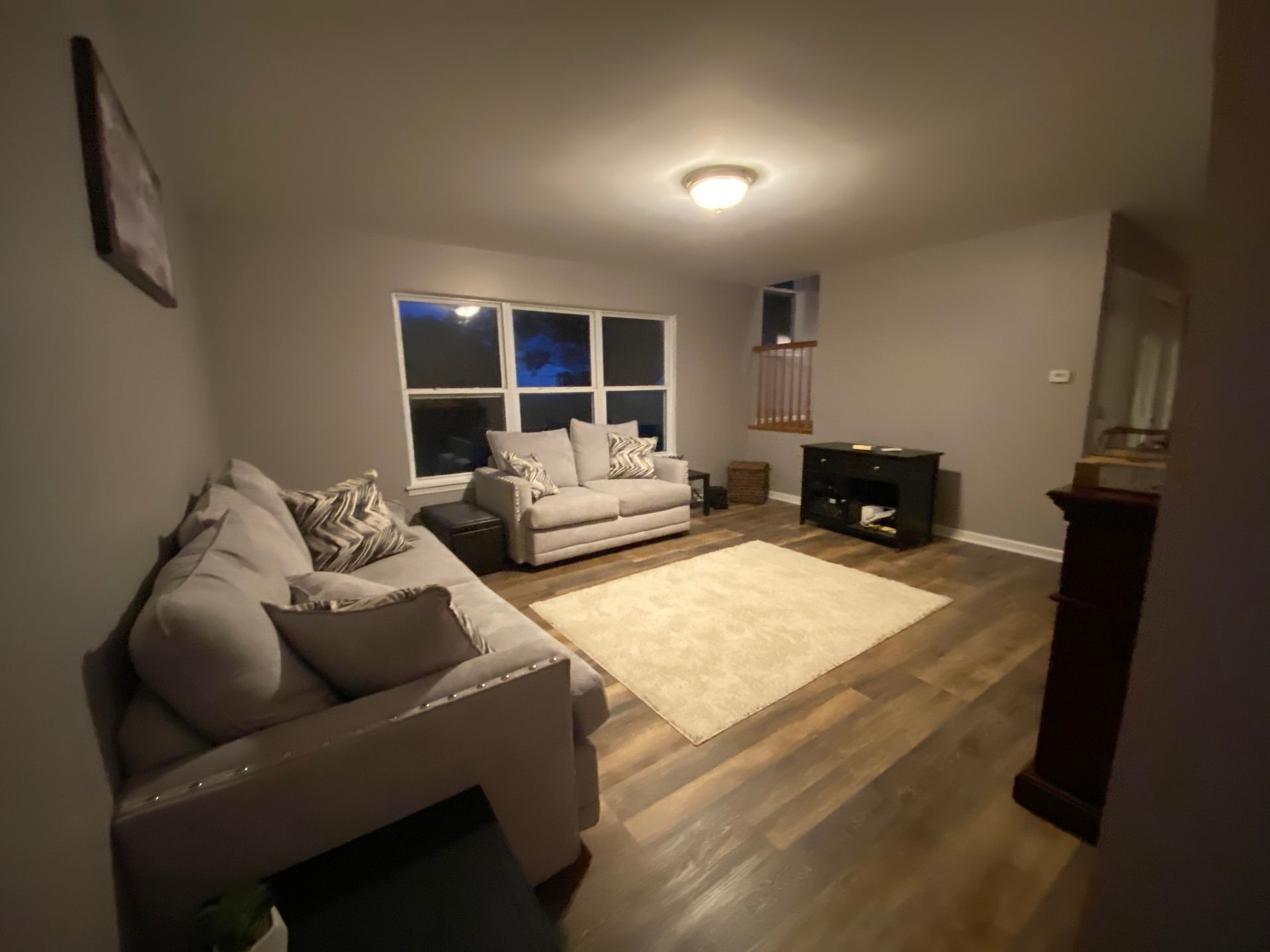 A living room with light gray walls, wooden floors, a beige rug, a gray sectional sofa, and a matching loveseat.