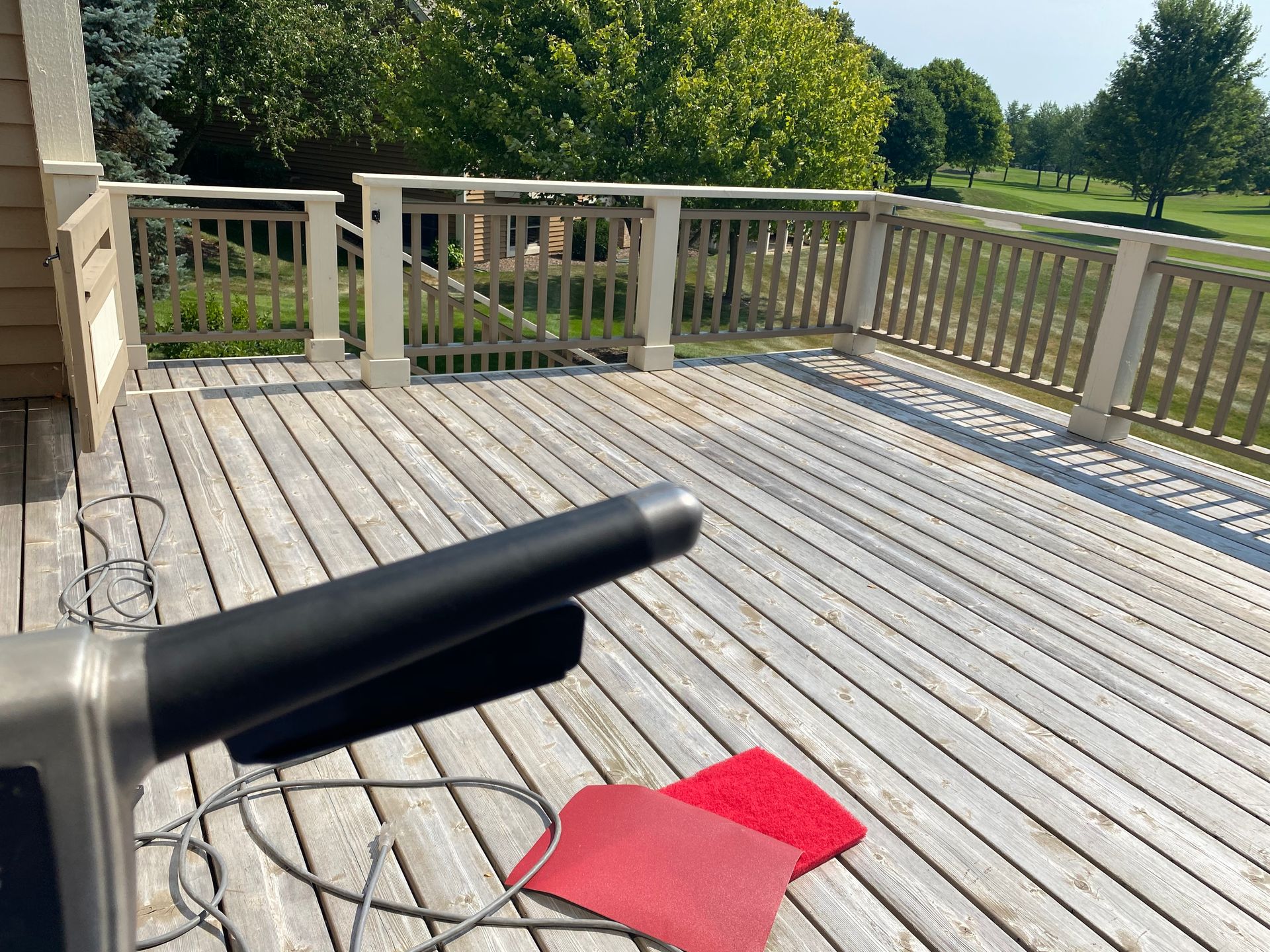 A wooden deck under construction, showing a sander handle in the foreground and red sanding pads on the deck boards.