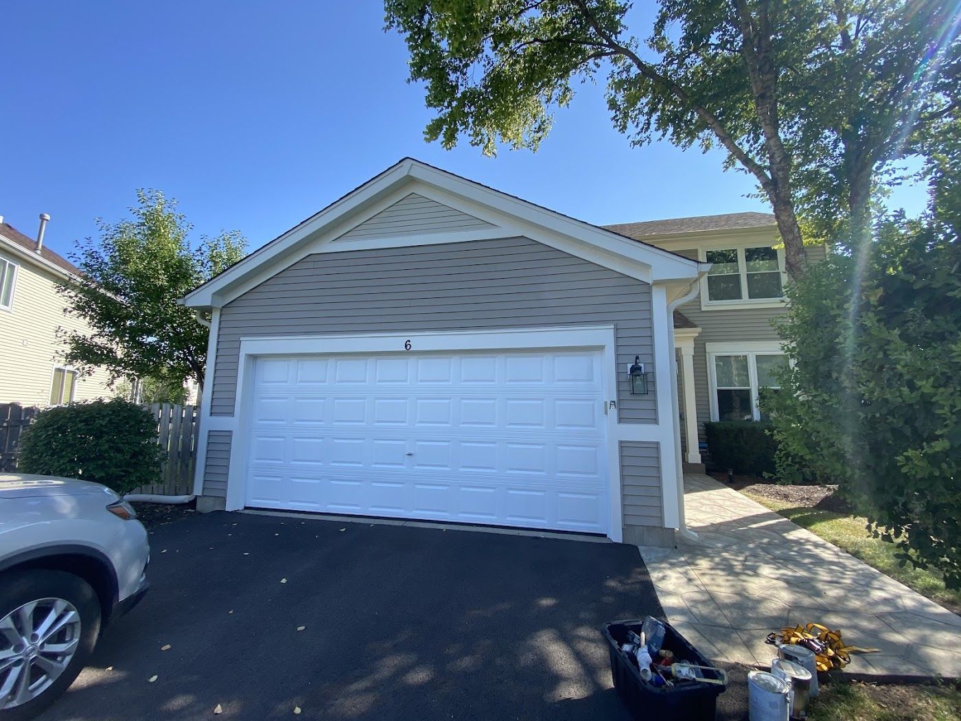 A light-gray suburban home with a white two-car garage, a paved driveway, and a path leading to the side entrance.