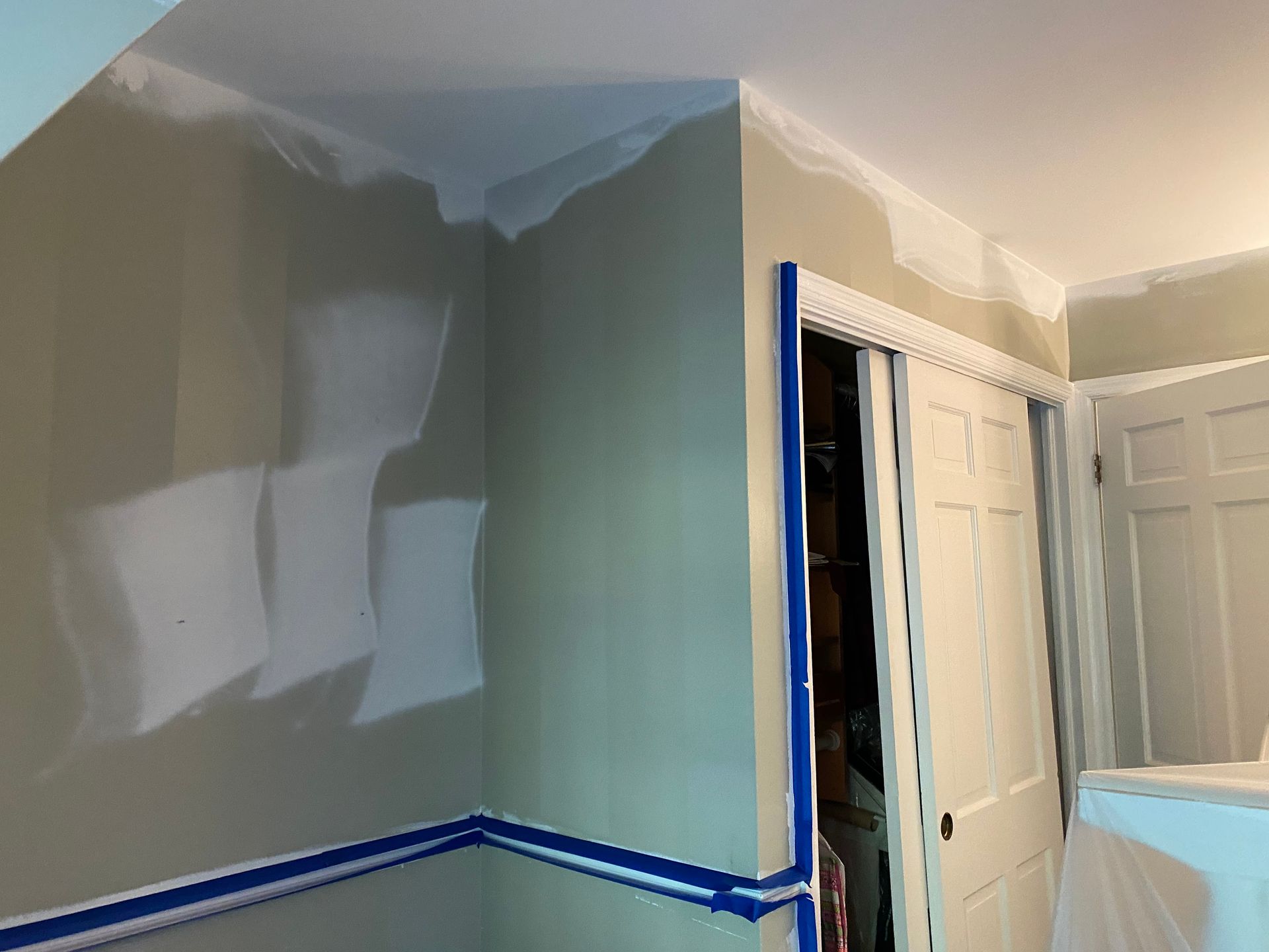 An interior room under construction with beige walls, fresh white paint patches, and blue painter's tape along the trim.