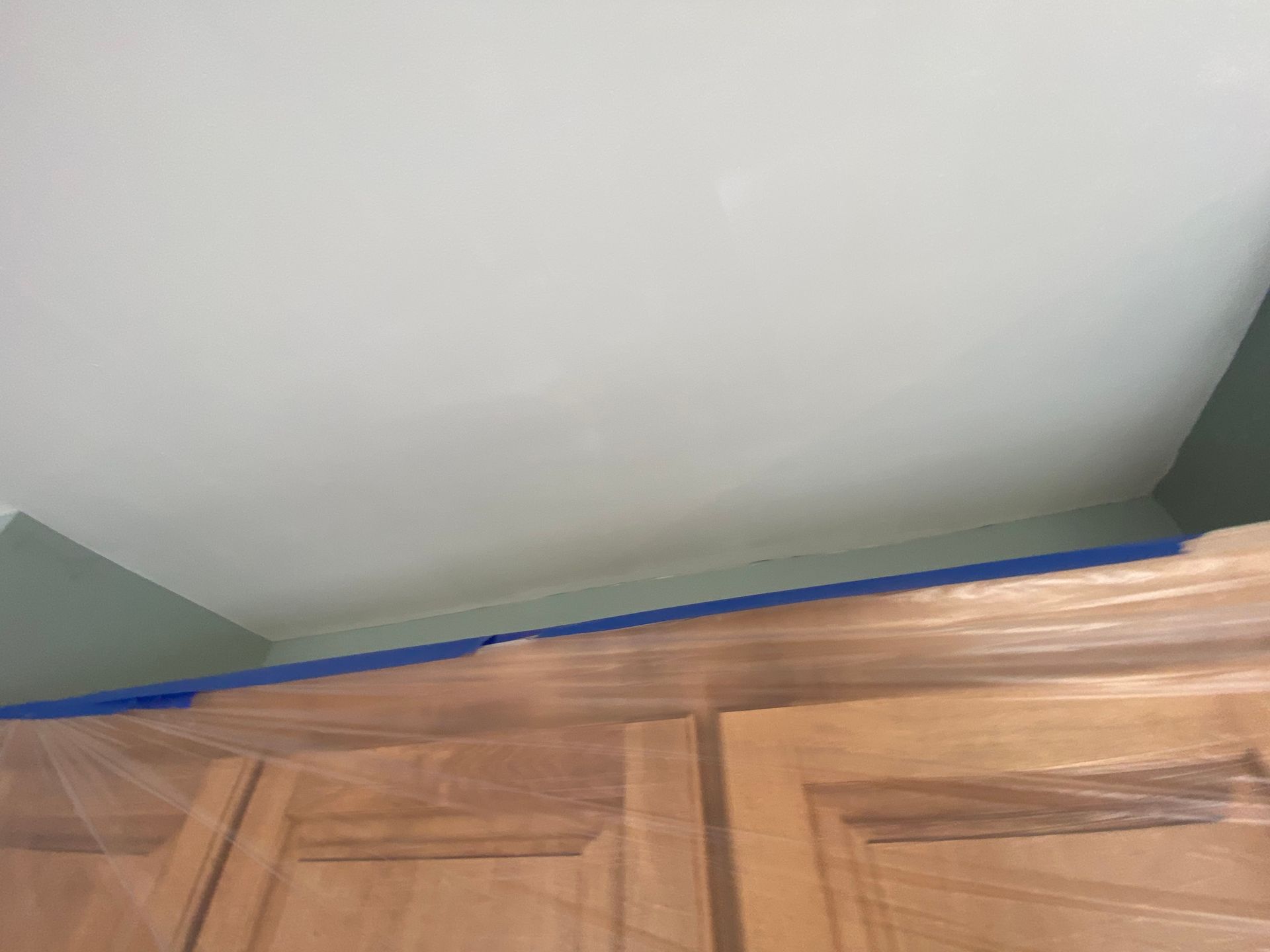 A top-down view of wooden kitchen cabinets with blue painter's tape along the top edge, prepared for wall painting.