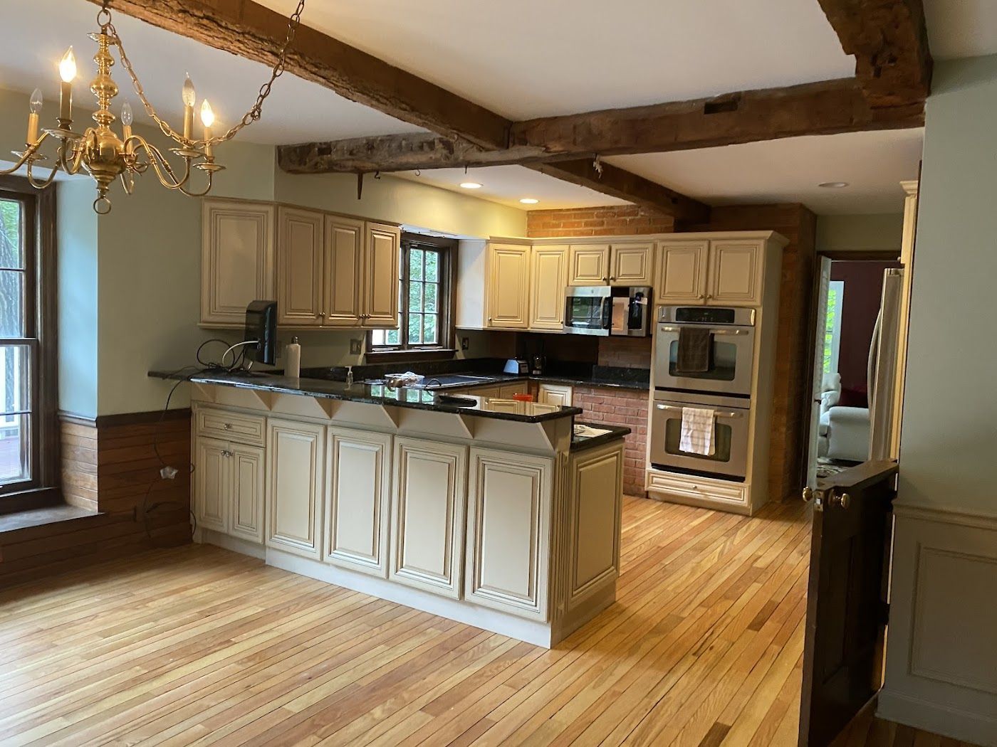 A kitchen with cream-colored cabinets, a granite countertop island, hardwood floors, and exposed wooden ceiling beams.