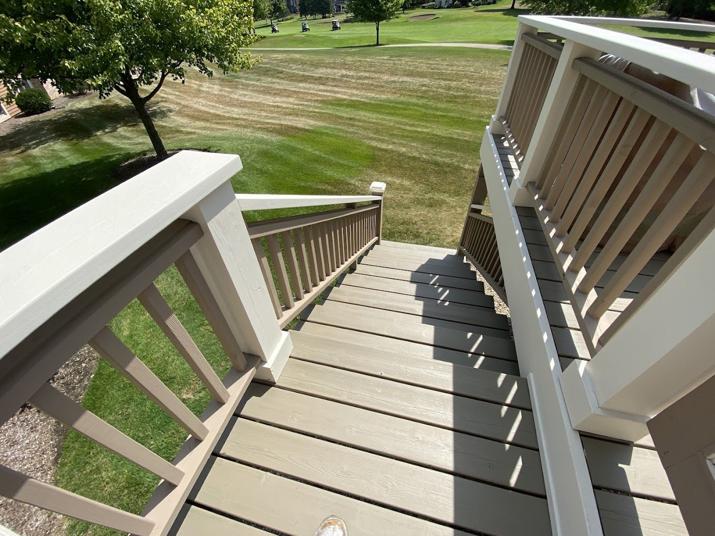 A high-angle view looking down a set of beige composite stairs with white railings, leading to a grassy lawn.