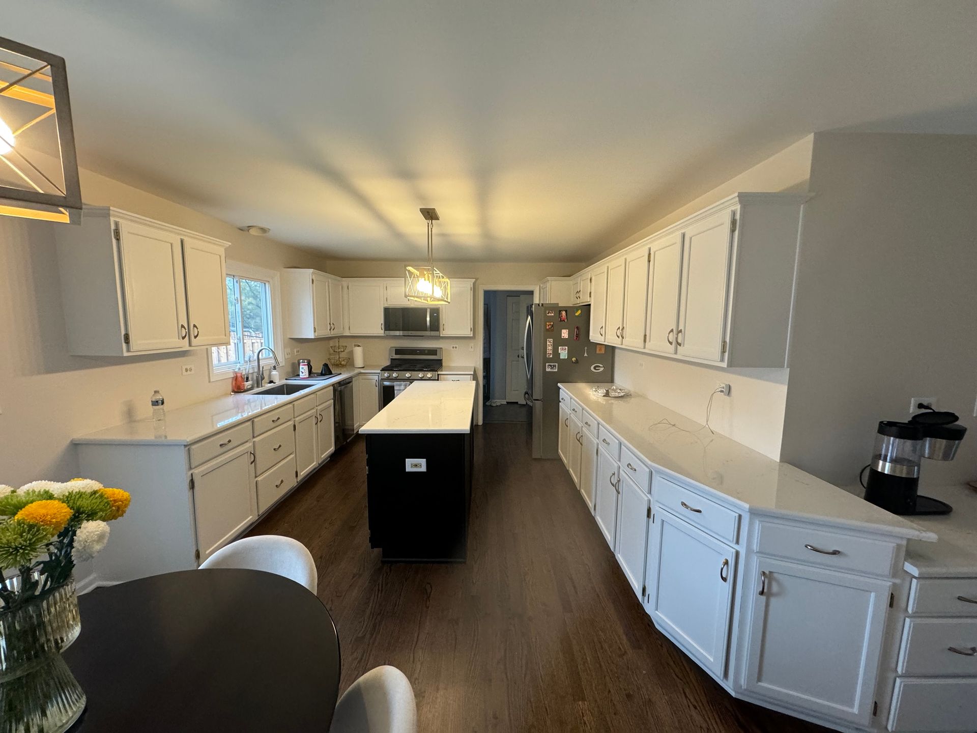 A kitchen with white cabinets, dark wood floors, a black kitchen island, and white countertops.