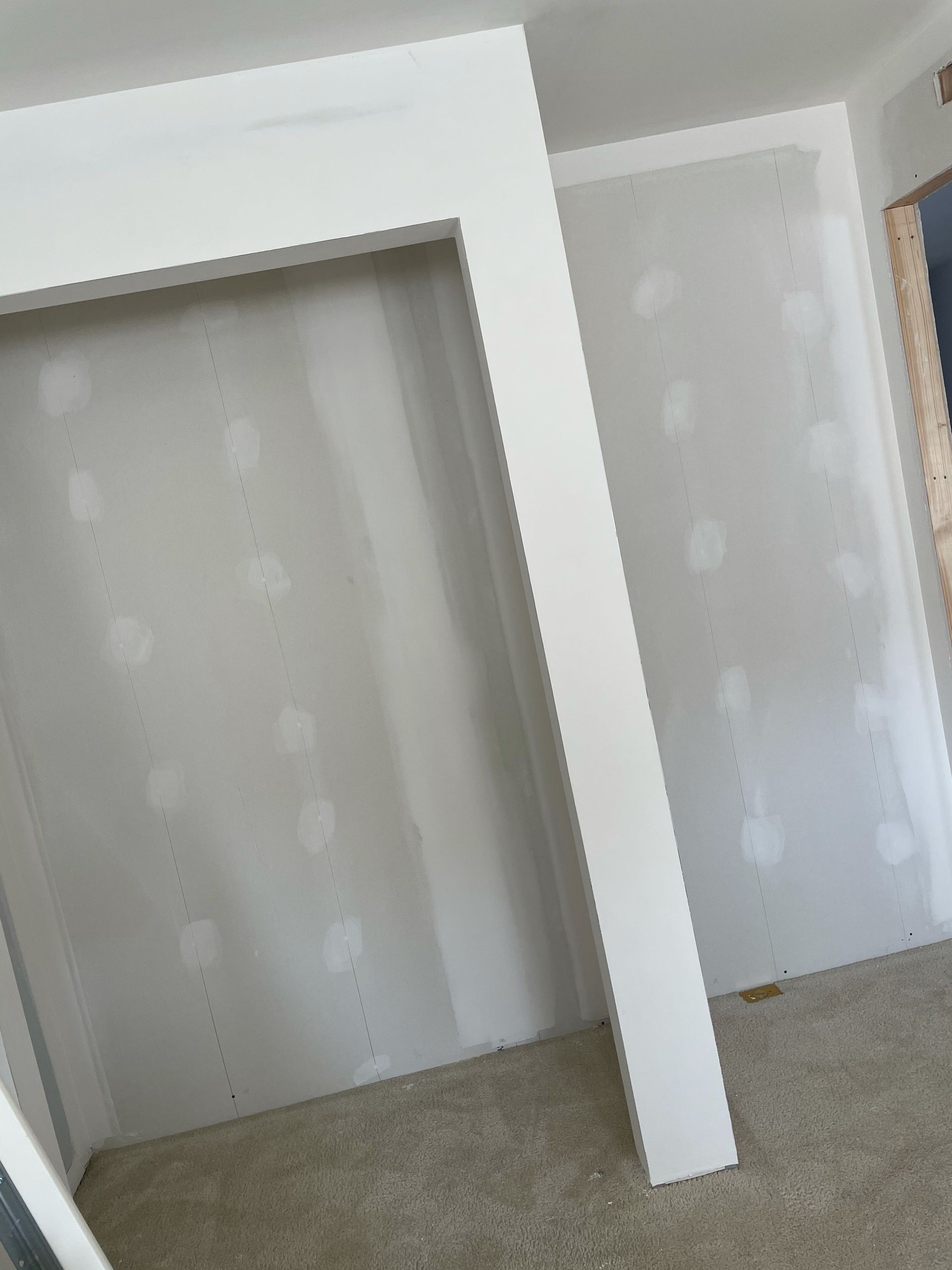 An unfinished interior room with a closet opening, showing bare drywall, spackled screw holes, and beige carpet.