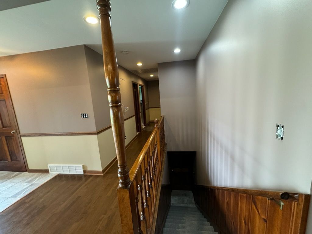 Interior hallway landing with wood banister, stairs, and beige walls in a home