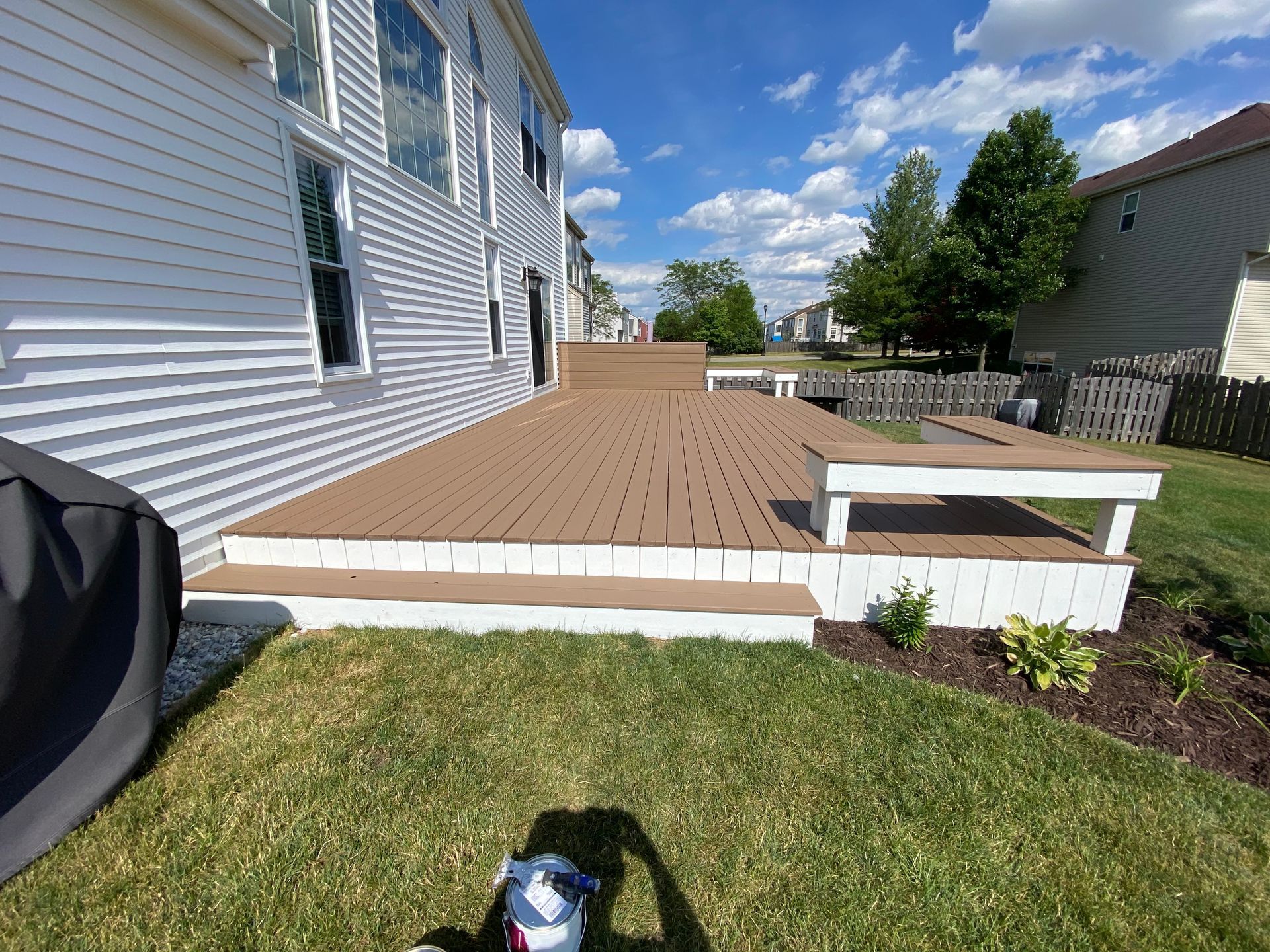 A tan backyard deck with white trim and a built-in bench attached to the side of a house with white siding and a lawn.
