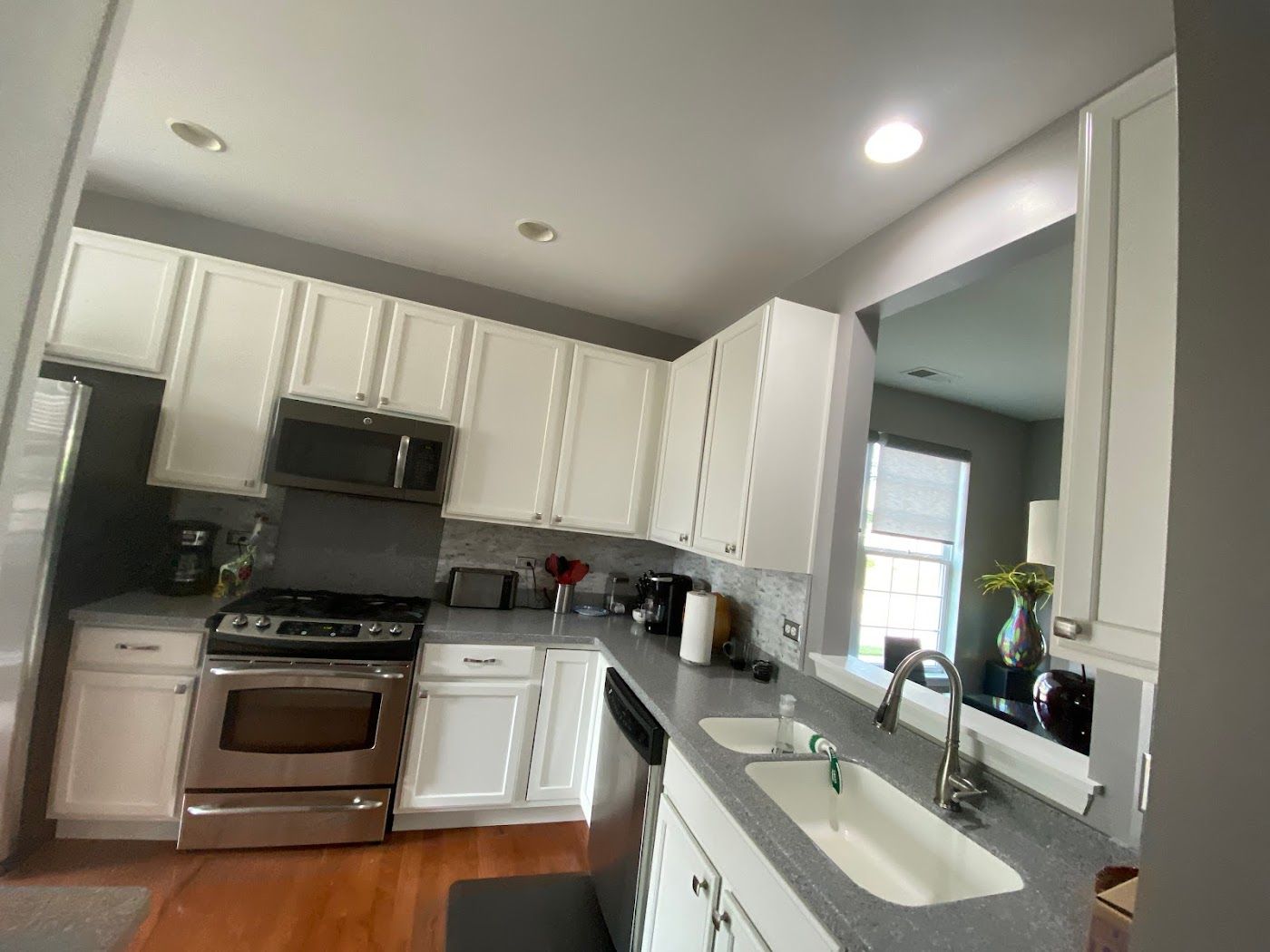 A modern kitchen with white cabinets, stainless steel appliances, grey countertops, and hardwood flooring.