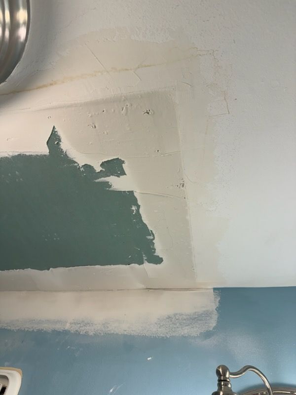 Partially painted bathroom wall with teal and white patches above a sink faucet