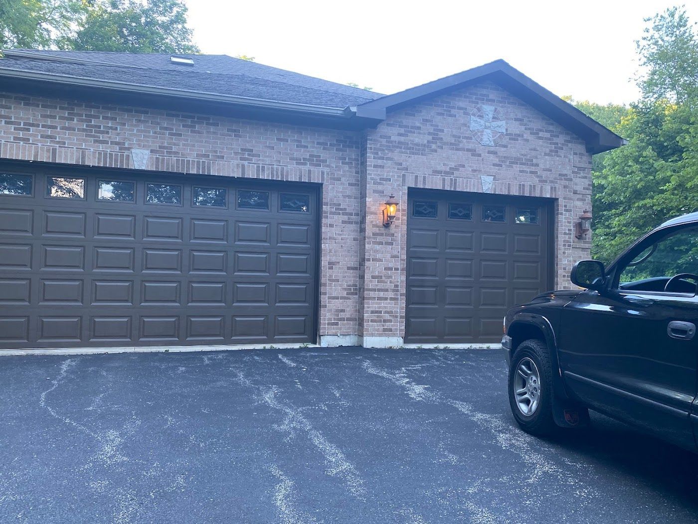 A brick house with a two-car garage and a single-car garage, with a dark pickup truck parked in the driveway.