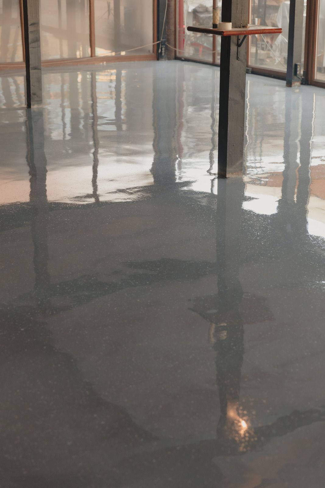 A dining area being prepped for painting, with floors covered in brown paper, furniture wrapped in plastic, and gray walls.