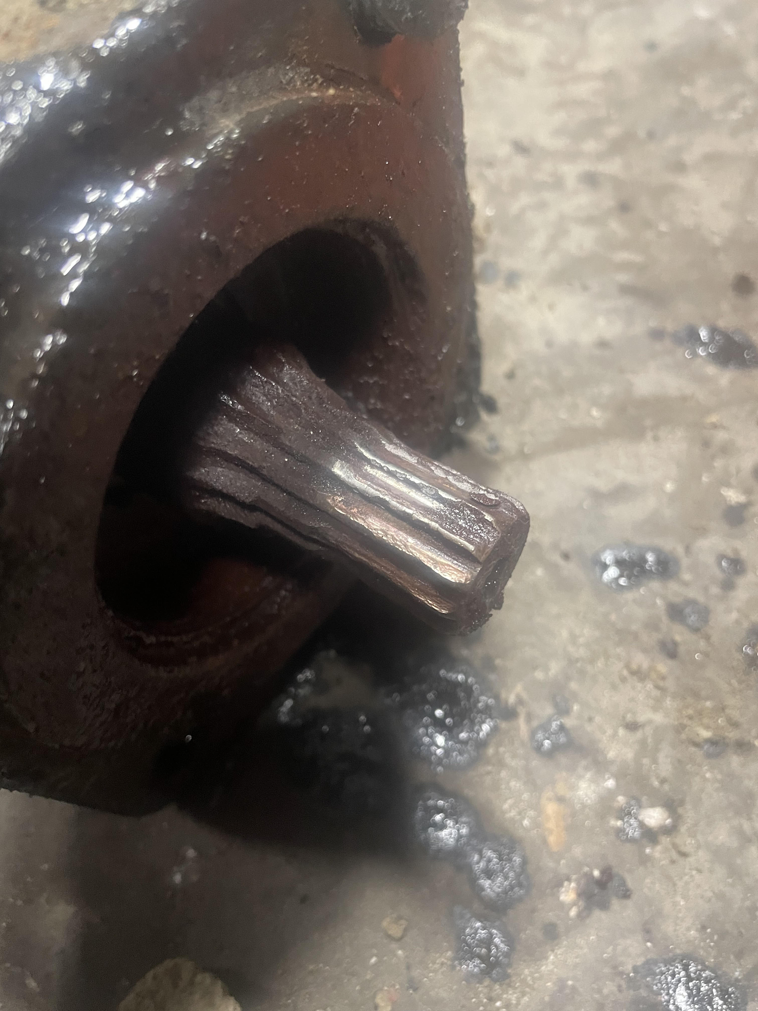 Close-up of a rusted, splined metal shaft protruding from a dark, oil-covered component.