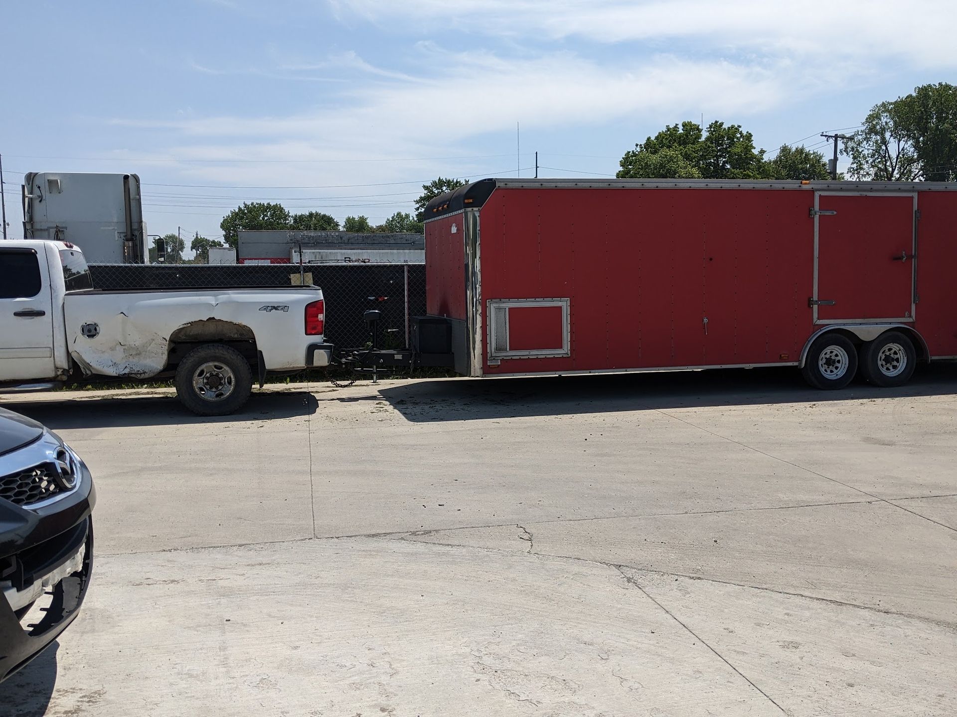 White truck towing a red trailer on a paved lot, sunny day.