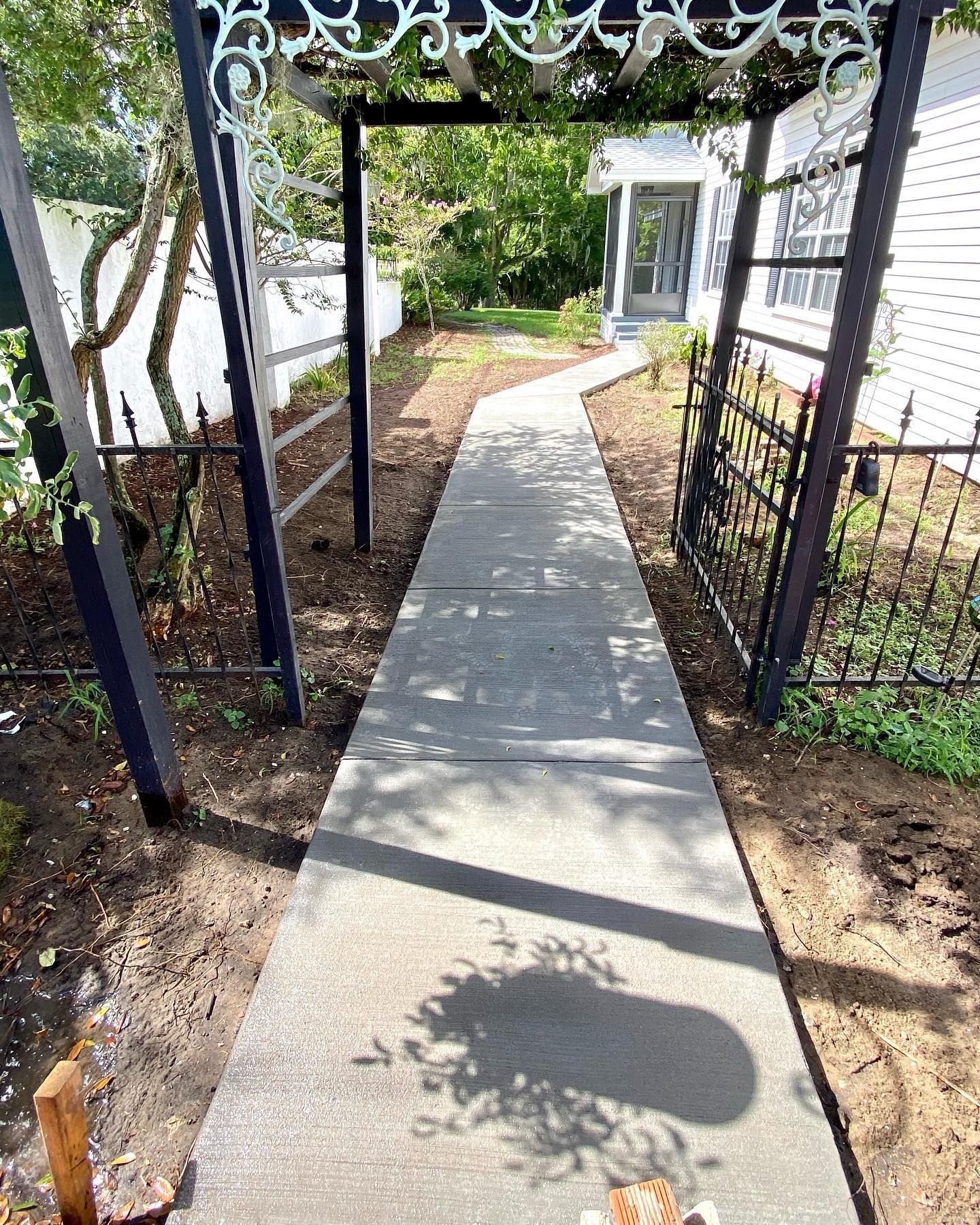 A concrete walkway leading to a house with a pergola.