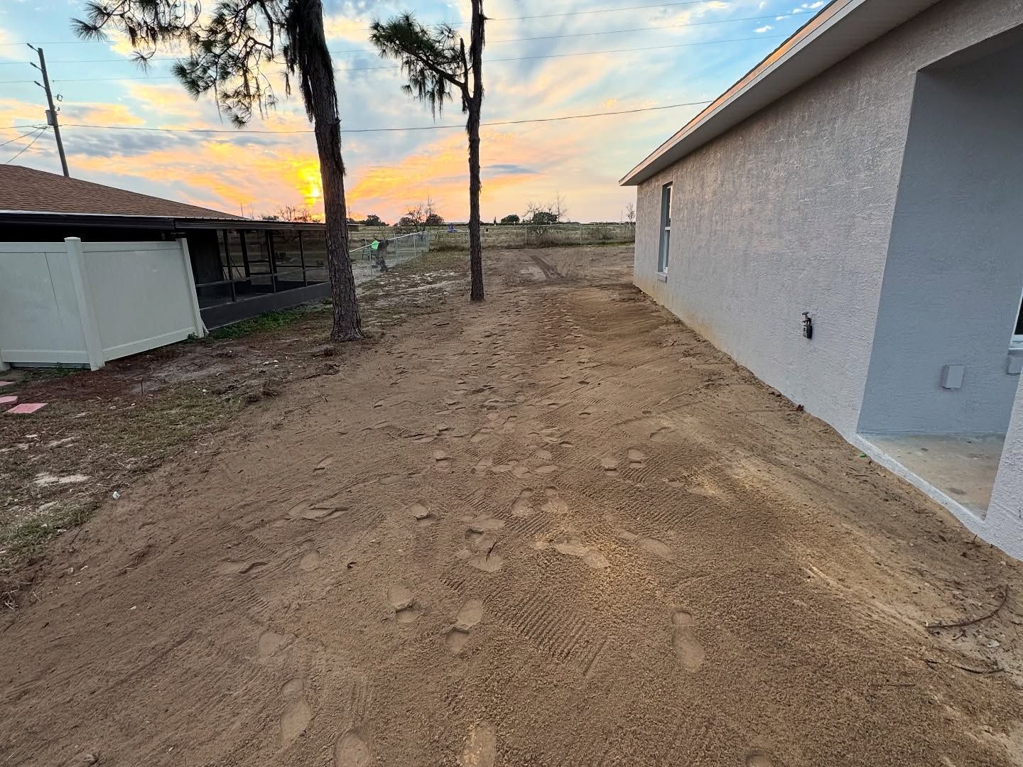 A dirt road leading to a house with a sunset in the background.
