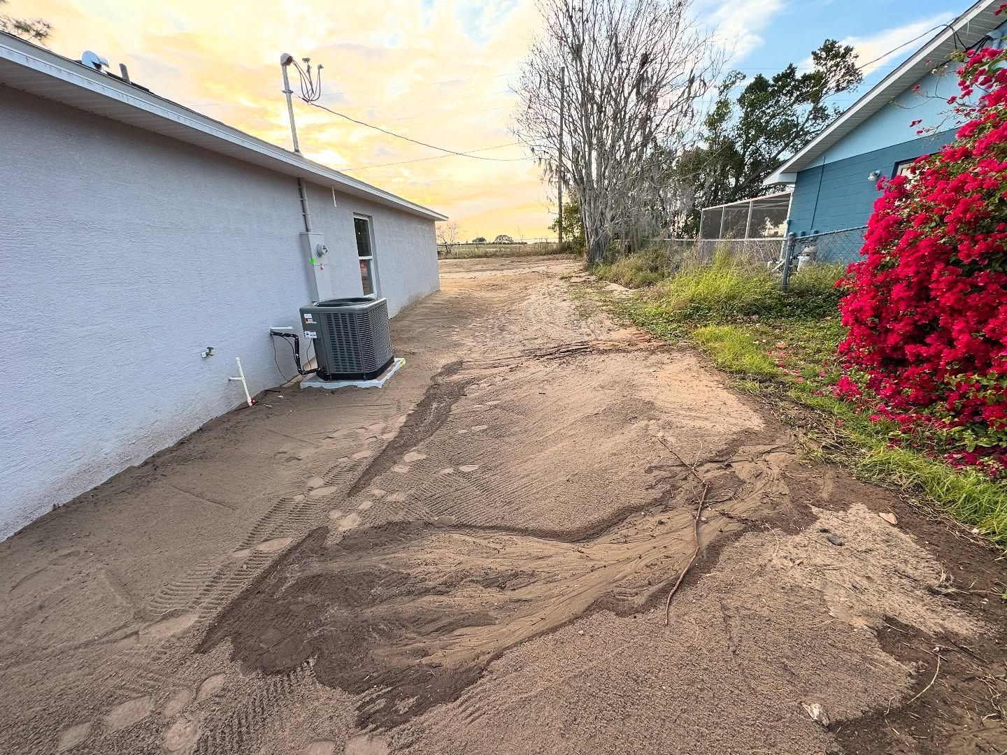 A dirt road leading to a house with flowers on the side of it.