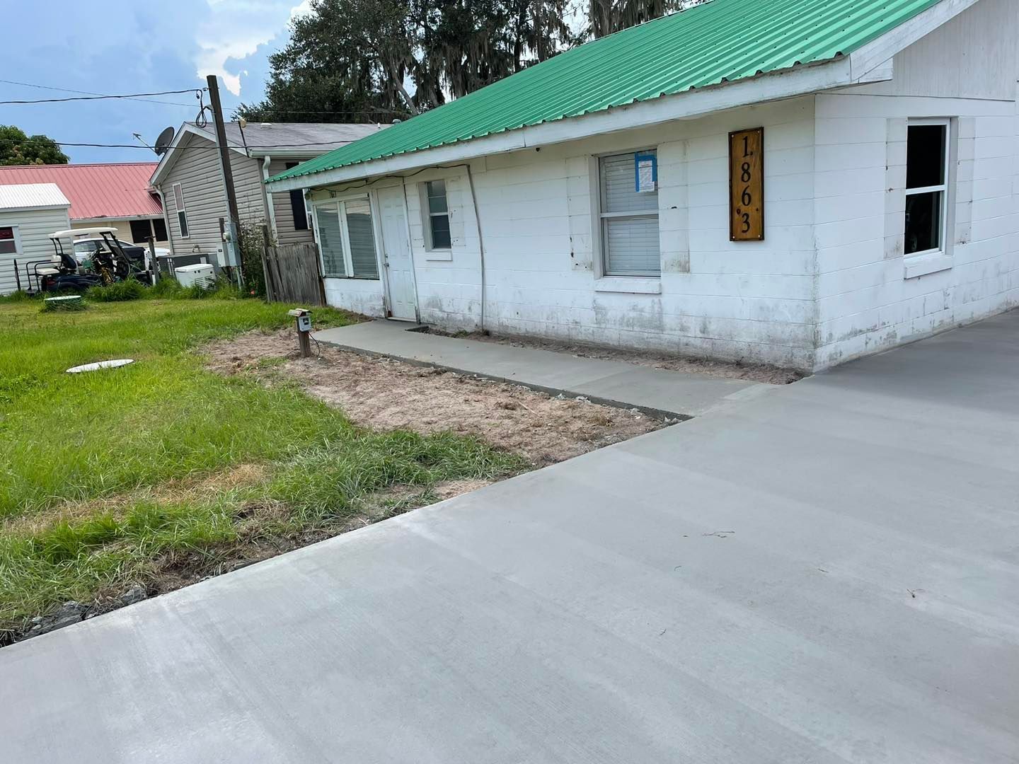 A white house with a green roof and a concrete driveway in front of it.
