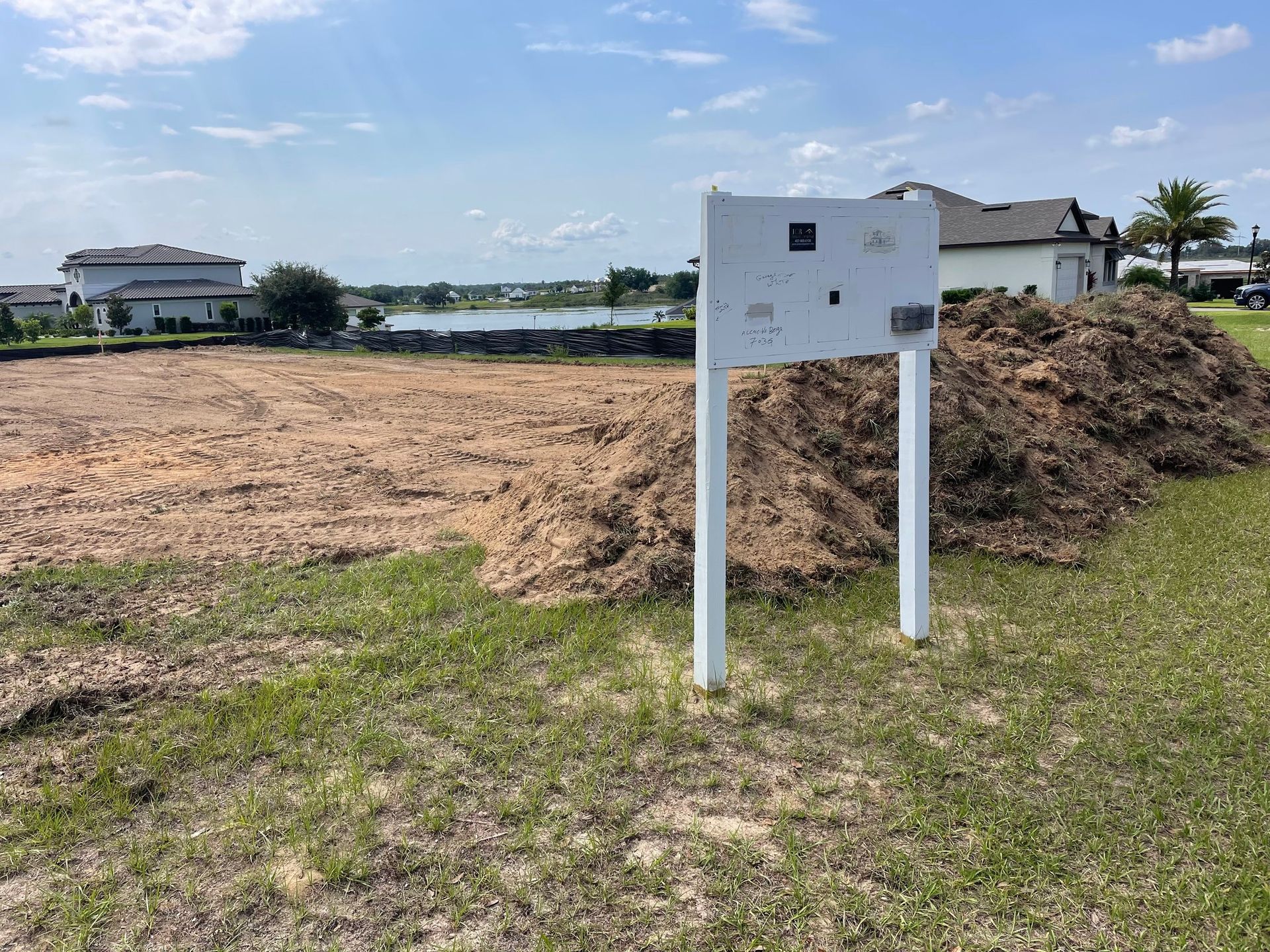A white sign is sitting in the middle of a field next to a pile of dirt.