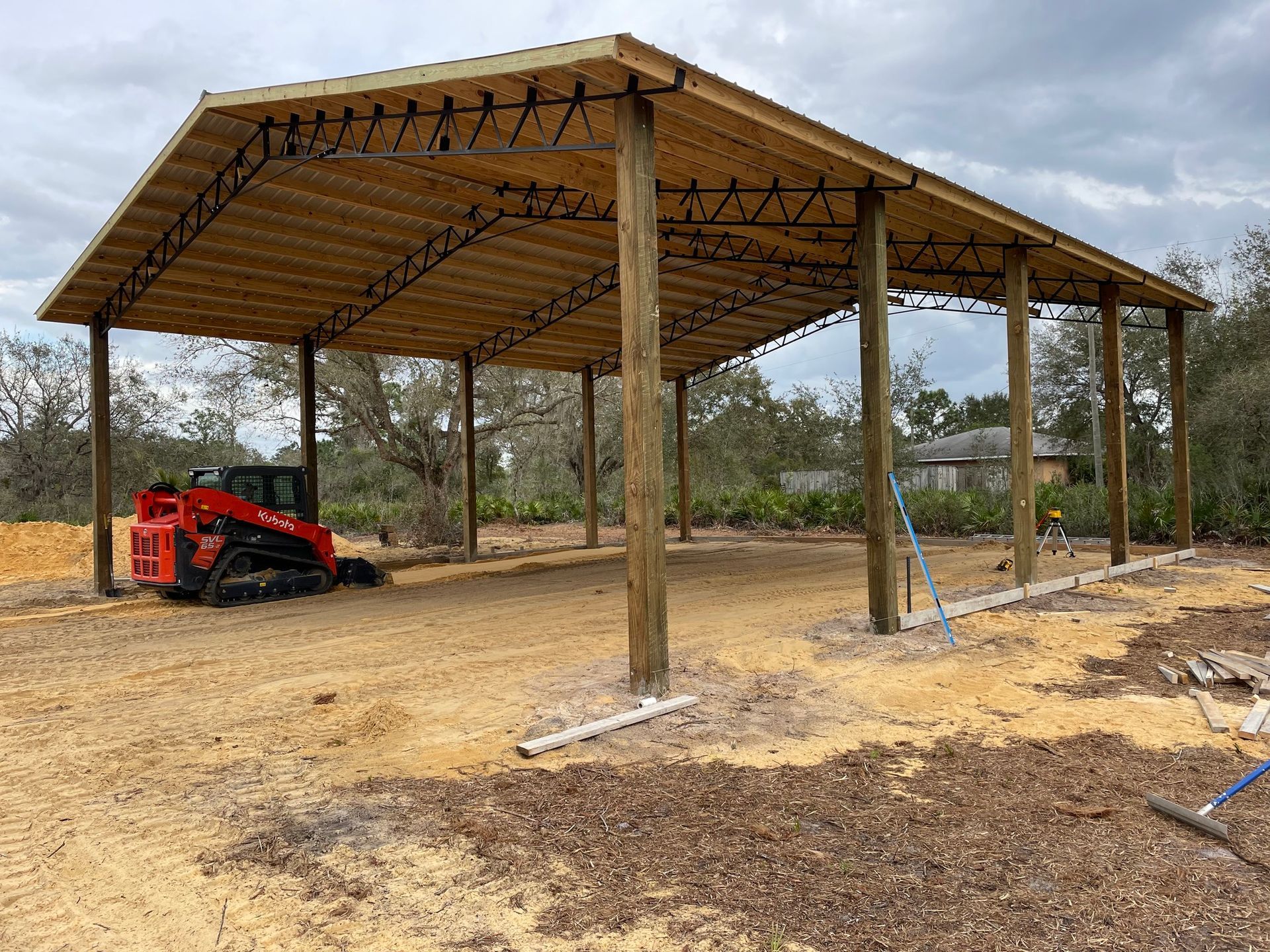 A red bulldozer is parked under a wooden structure.