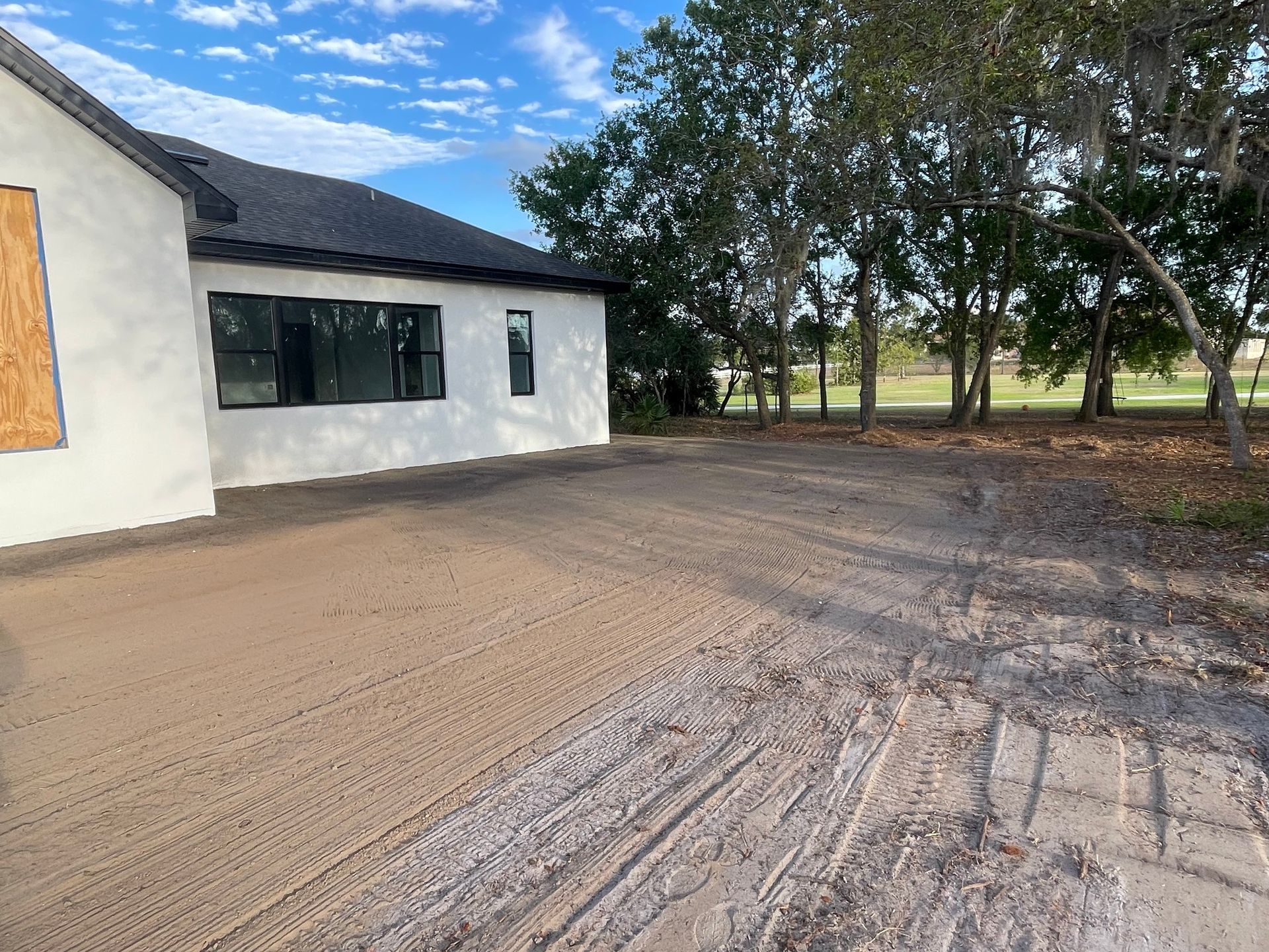 A white house with a black roof is sitting next to a dirt road.