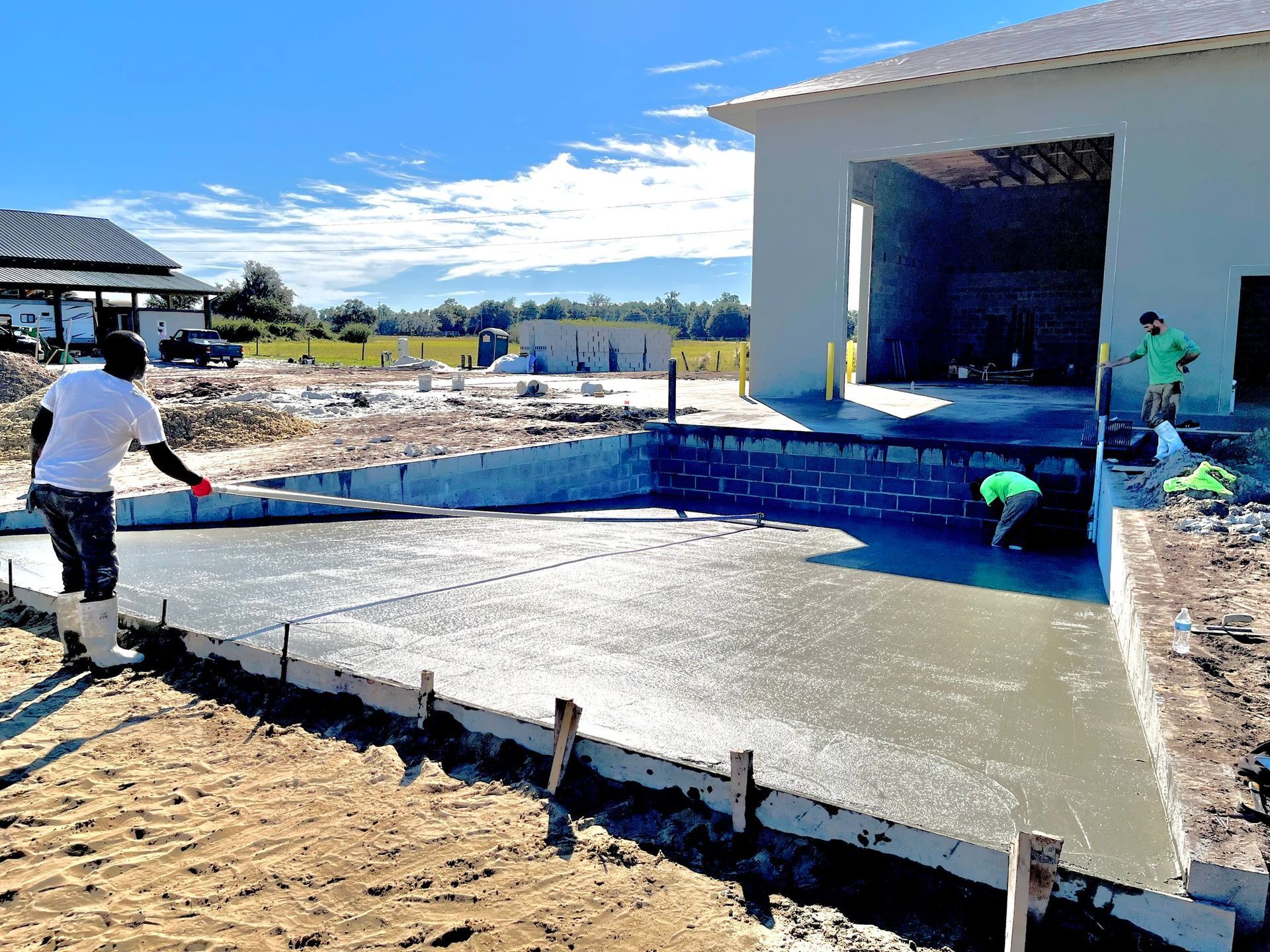 A man is pouring concrete in front of a building under construction.