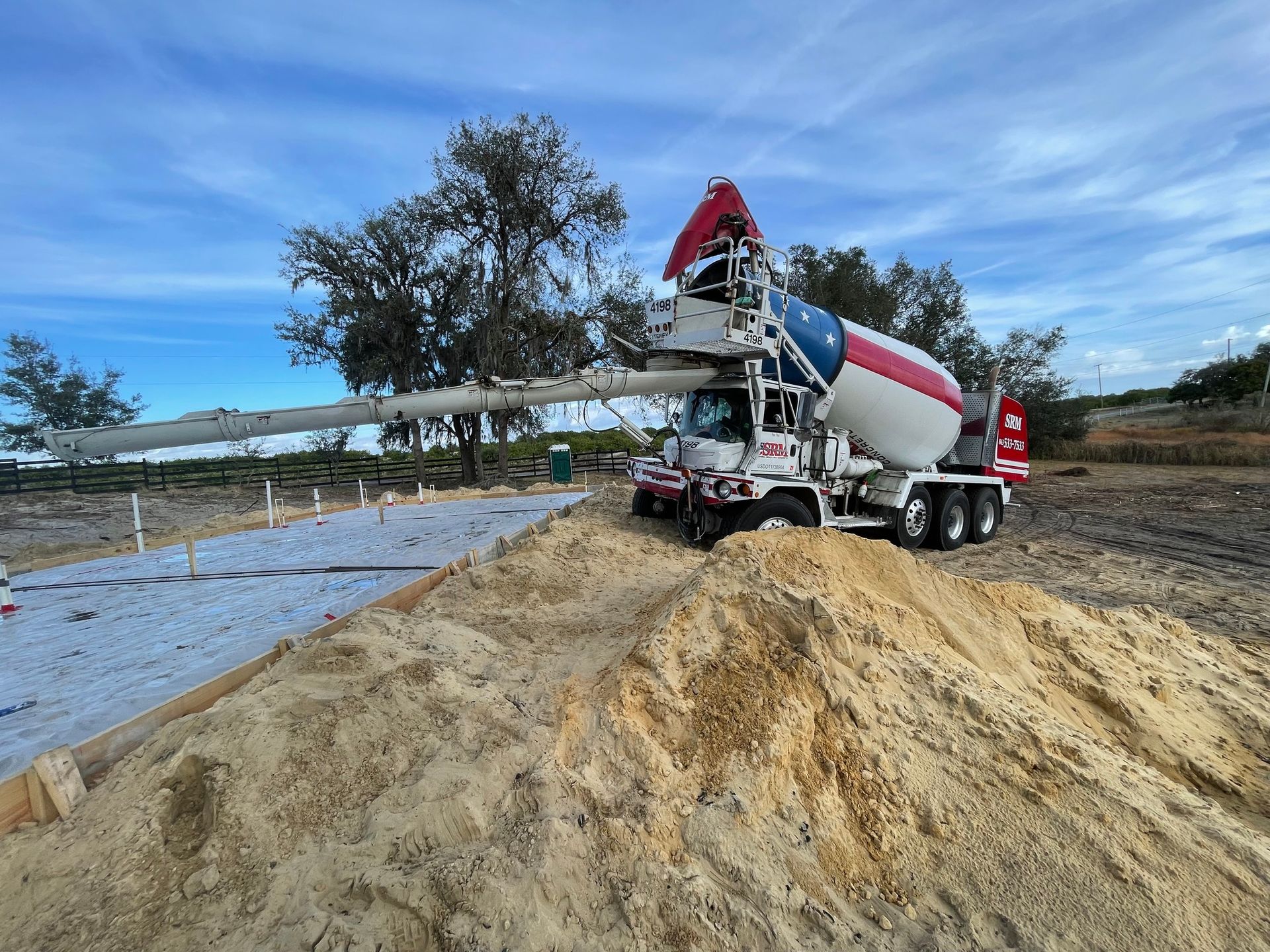 A concrete mixer truck is pouring concrete into a pile of sand.