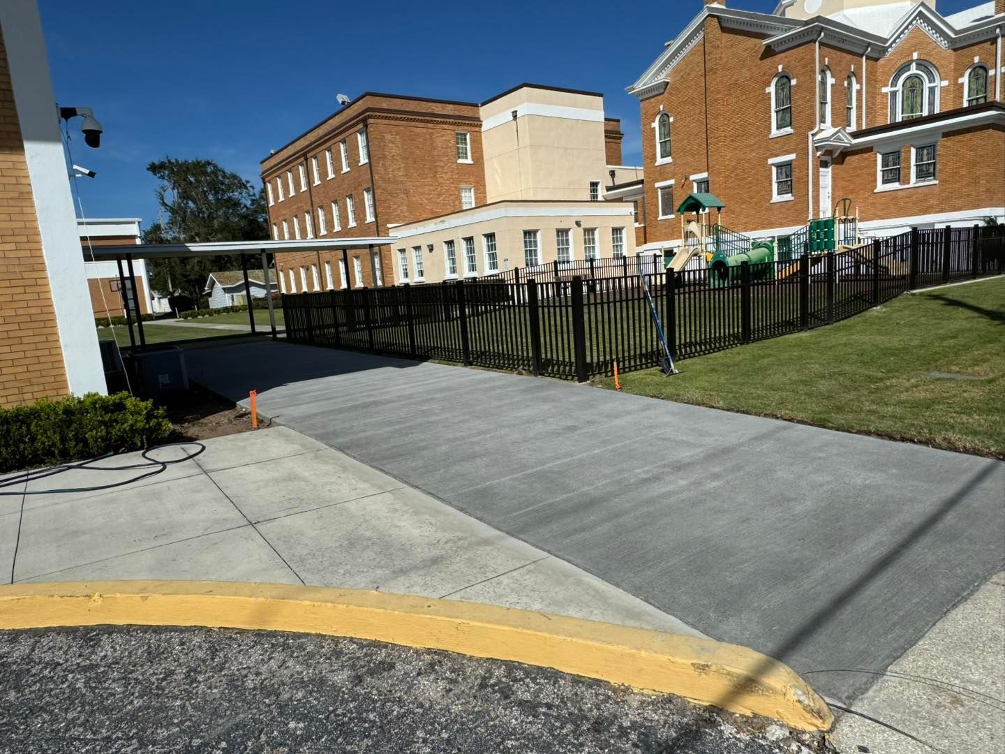 A brick building is behind a concrete walkway with a yellow curb.