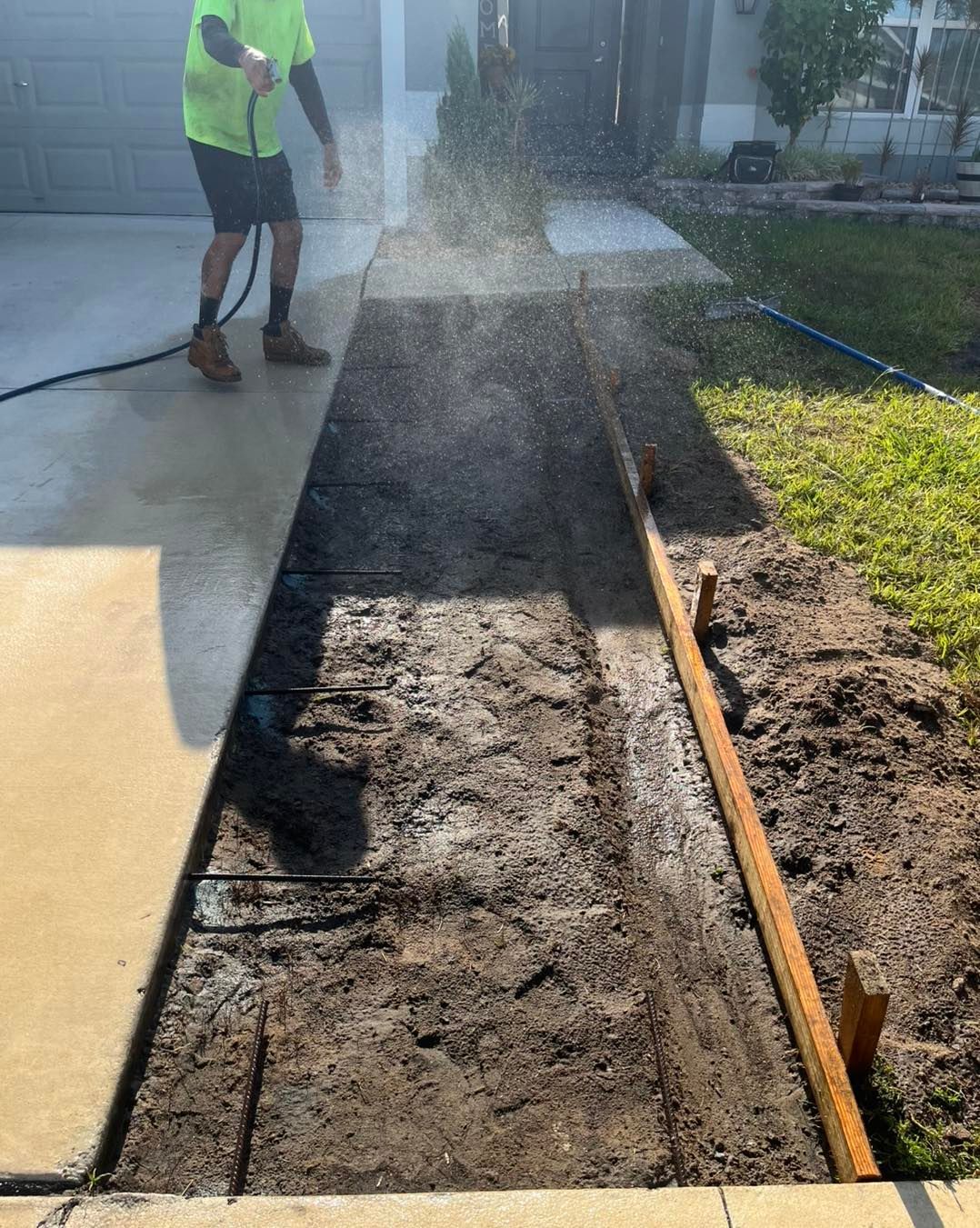 A man is cleaning a sidewalk with a hose.