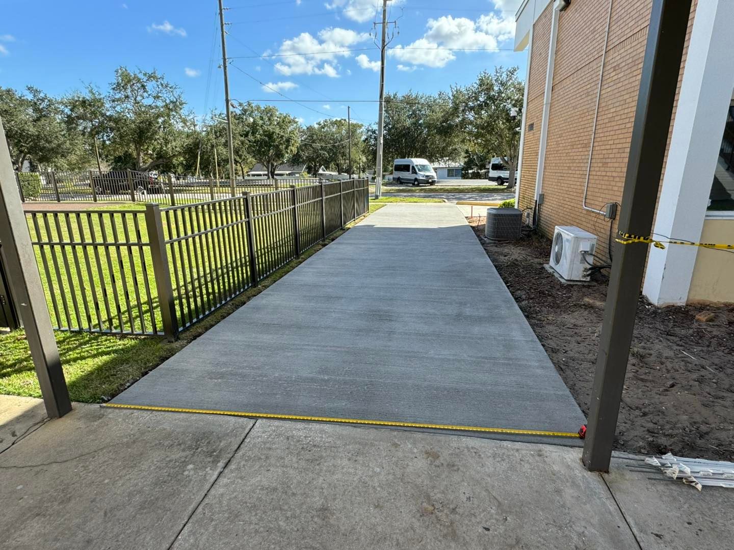 A concrete walkway leading to a building next to a fence.