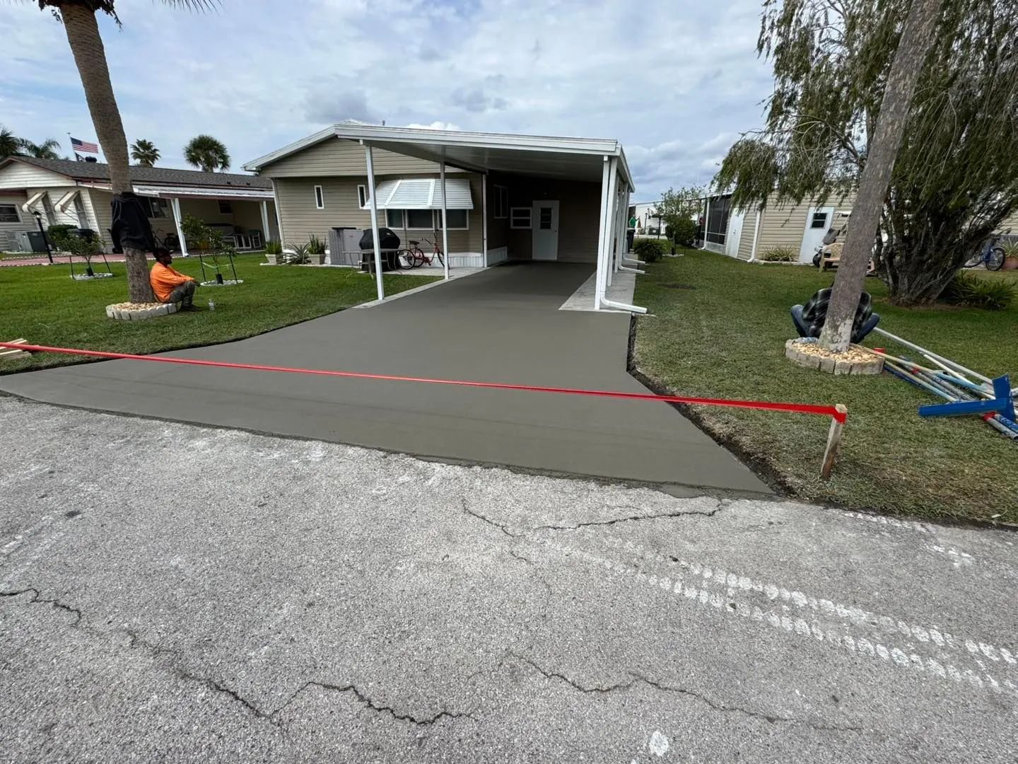 Freshly poured concrete driveway in front of a mobile home with a carport.