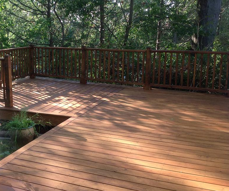 A wooden deck with a wooden railing and trees in the background.