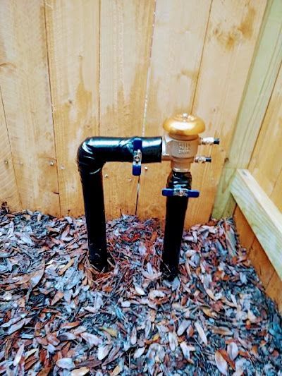 A black pipe is sitting on top of a pile of leaves in front of a wooden fence.