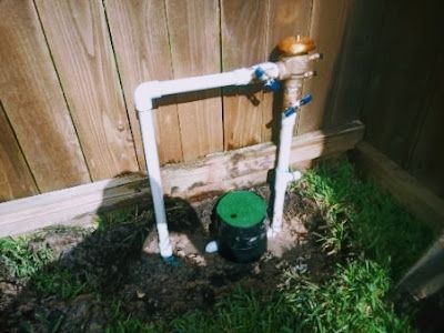 A water meter is sitting in the dirt next to a wooden fence.